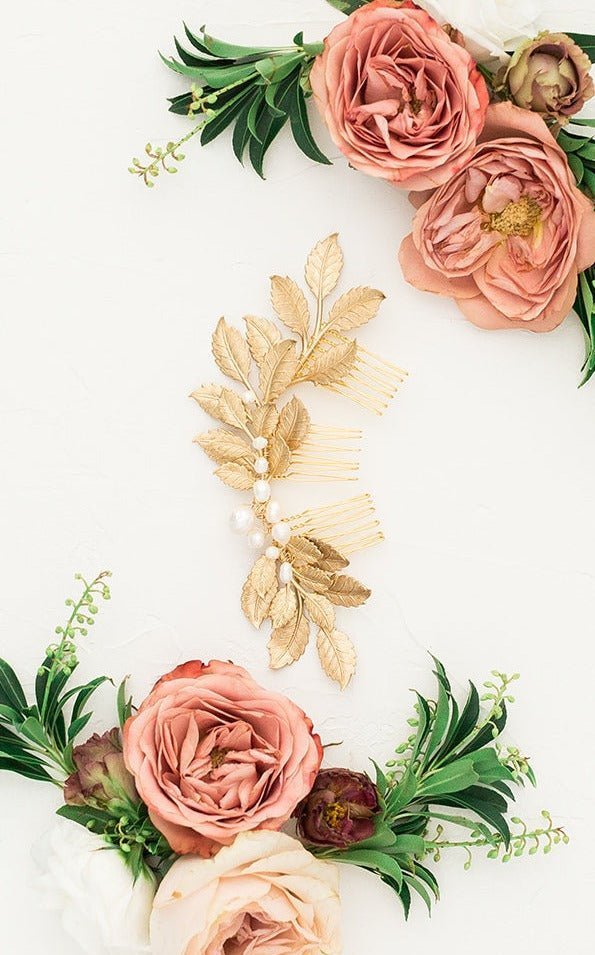 A three combed leafy golden bridal hairpiece with freshwater pearls between several dusty pink roses with greenery on a white background. Bridal hair accessories & Pearl bridal accessories by Canadian jewelry artist