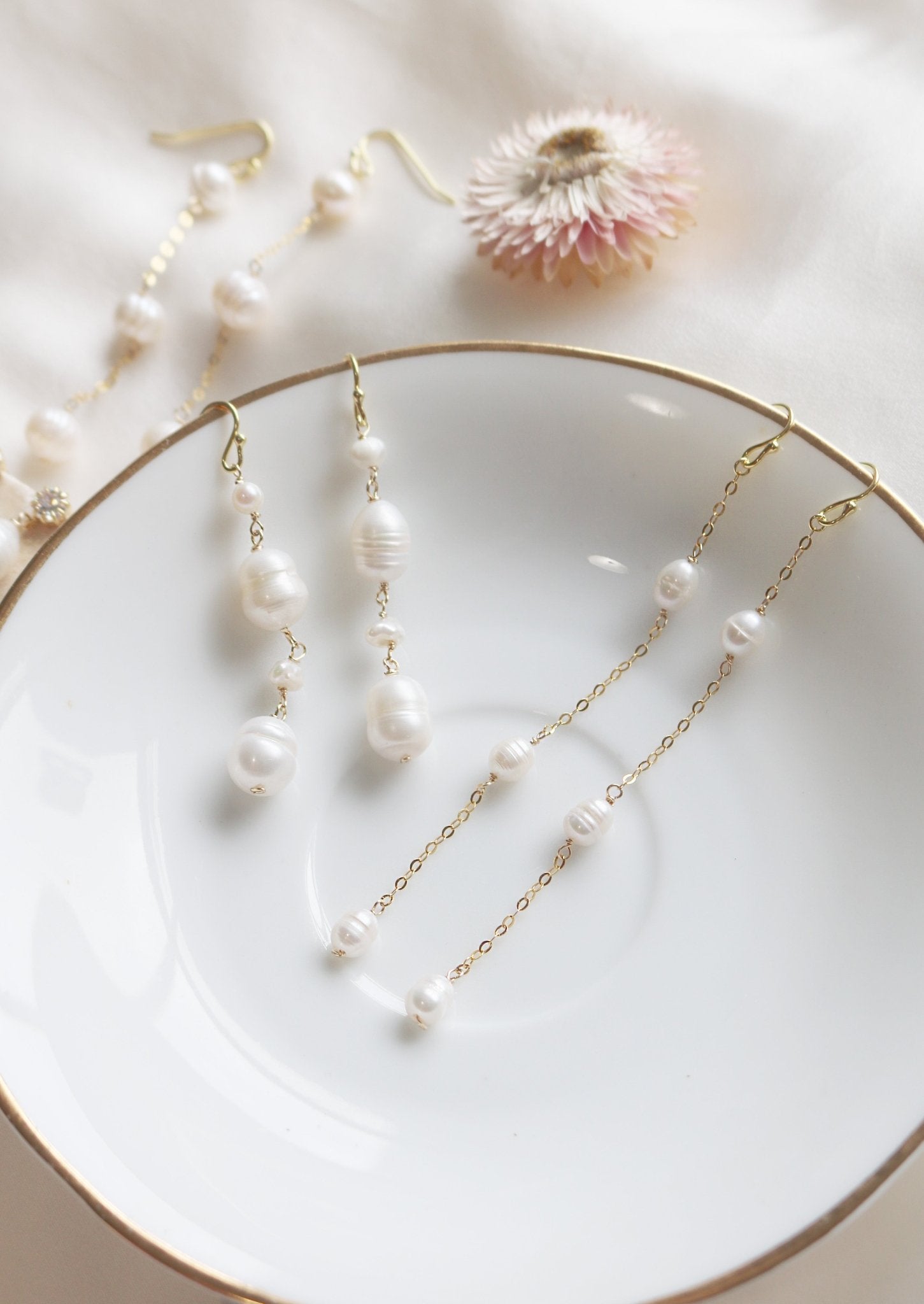 Two sets of gold-filled dangle earrings lay on a white plate, dripping with freshwater pearls. Organic pearl jewelry. Bridal jewelry Canada. Pearl jewelry Canada. Pearl Bridal jewelry Canada. Gold-filled jewelry Canada. Canadian jewelry brands. Canadian jewelry designs. Handmade Canadian jewelry.