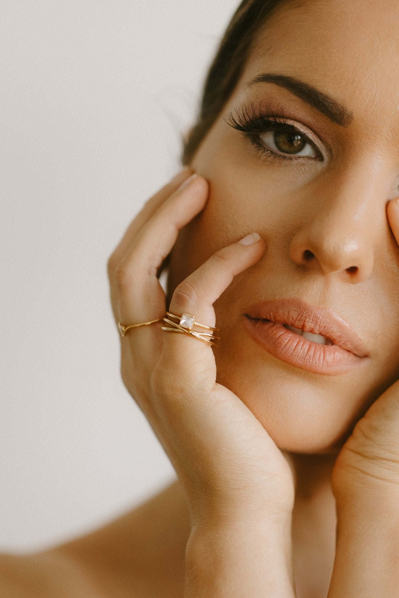 Close-up of a woman's face with one hand on her cheek, wearing 3 gold rings. Minimalist Jewelry. Canadian jewelry brands.