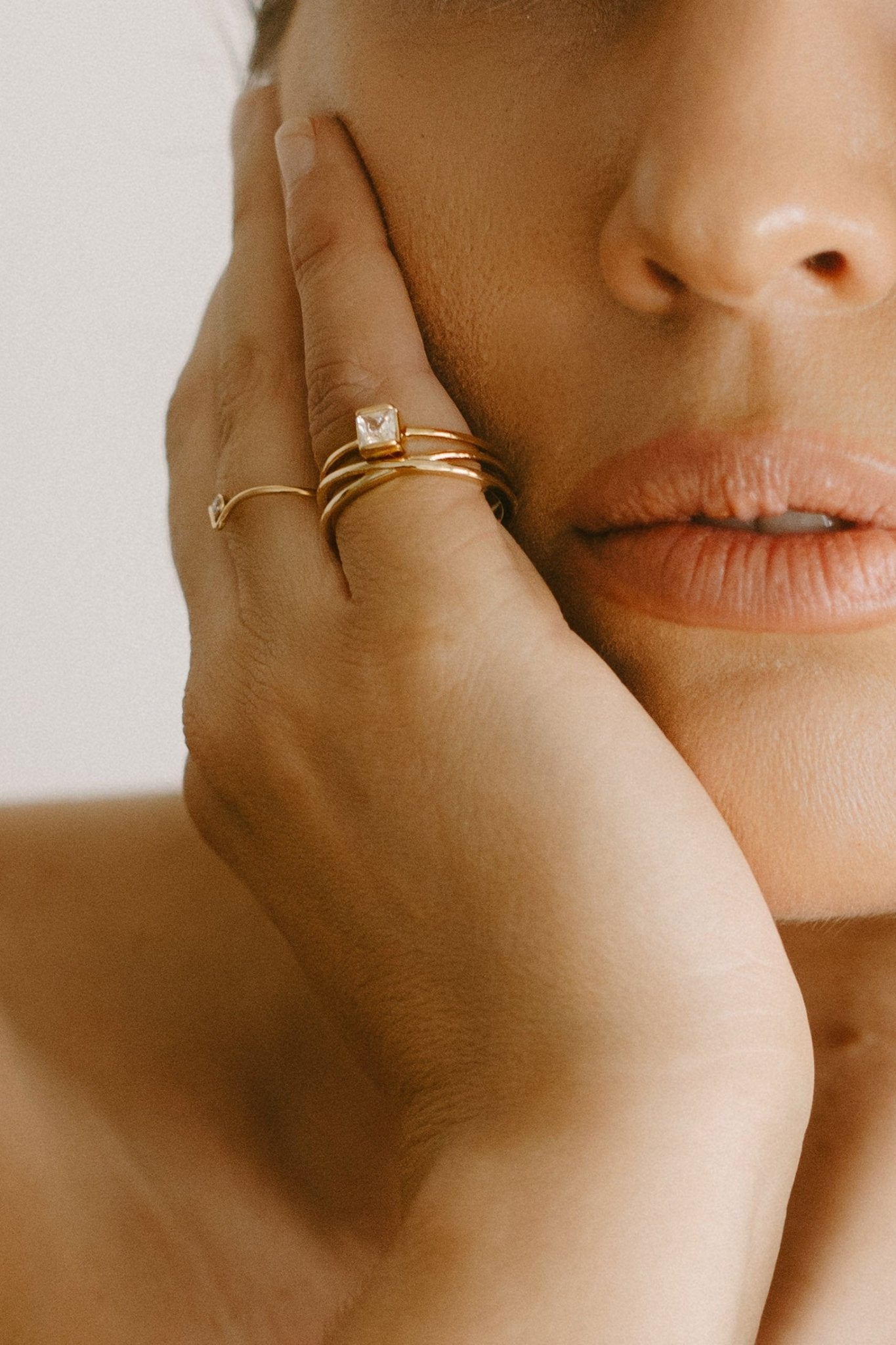 Close up of several modern jewelry rings stacked on fingers with hand near face. Small Canadian jewelry brands. Gold-filled jewelry Canada.