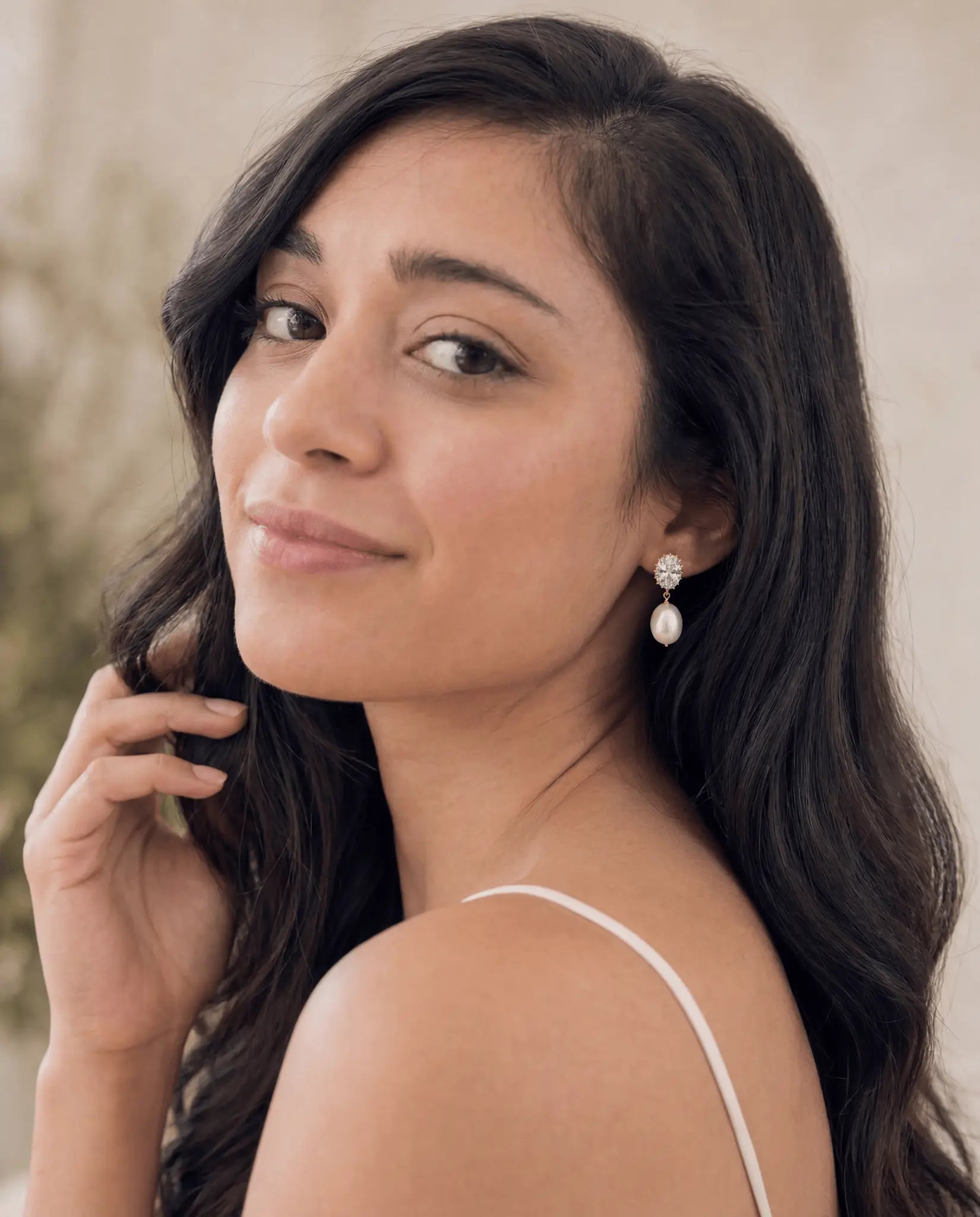 Filipino woman with long brown hair wearing crystal studded pearl drop earrings with a neutral background. Handmade pearl earrings by Canadian jewellery designer