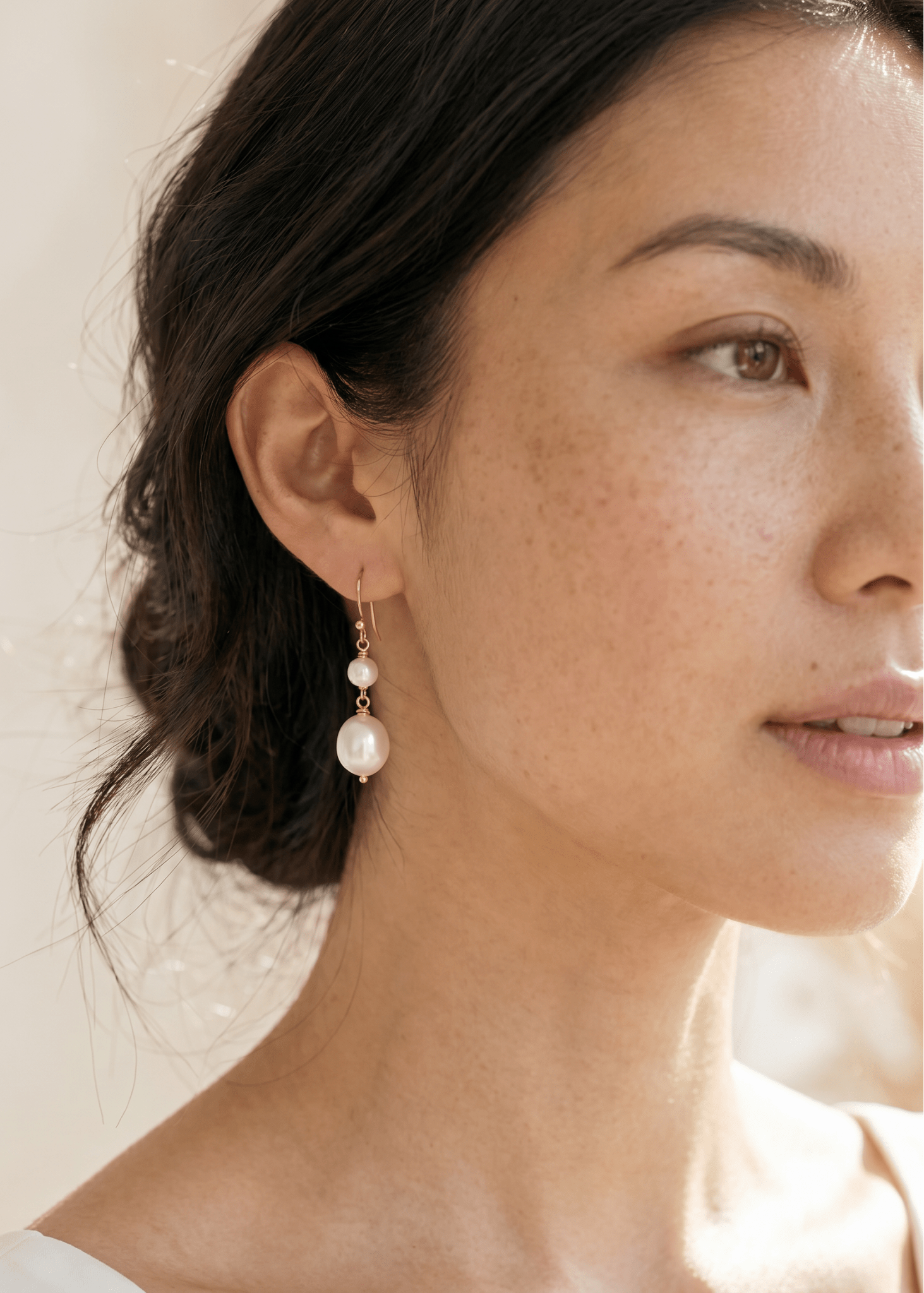 Close up of pearl drop earrings in gold filled on BIPOC model against neutral background.
