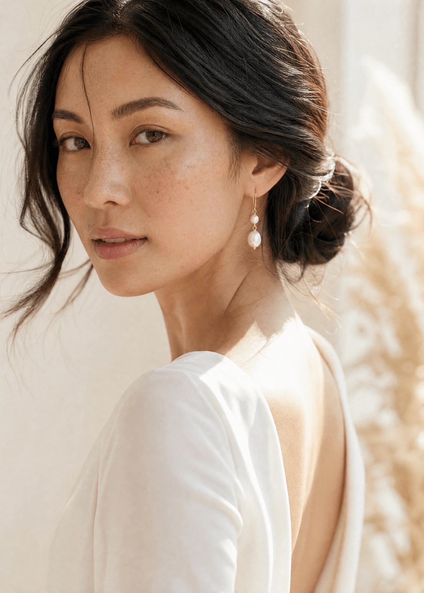 Filipino woman in white wearing handmade gold fresh water pearl drop earrings by BIPOC jewelry designer against neutral background.