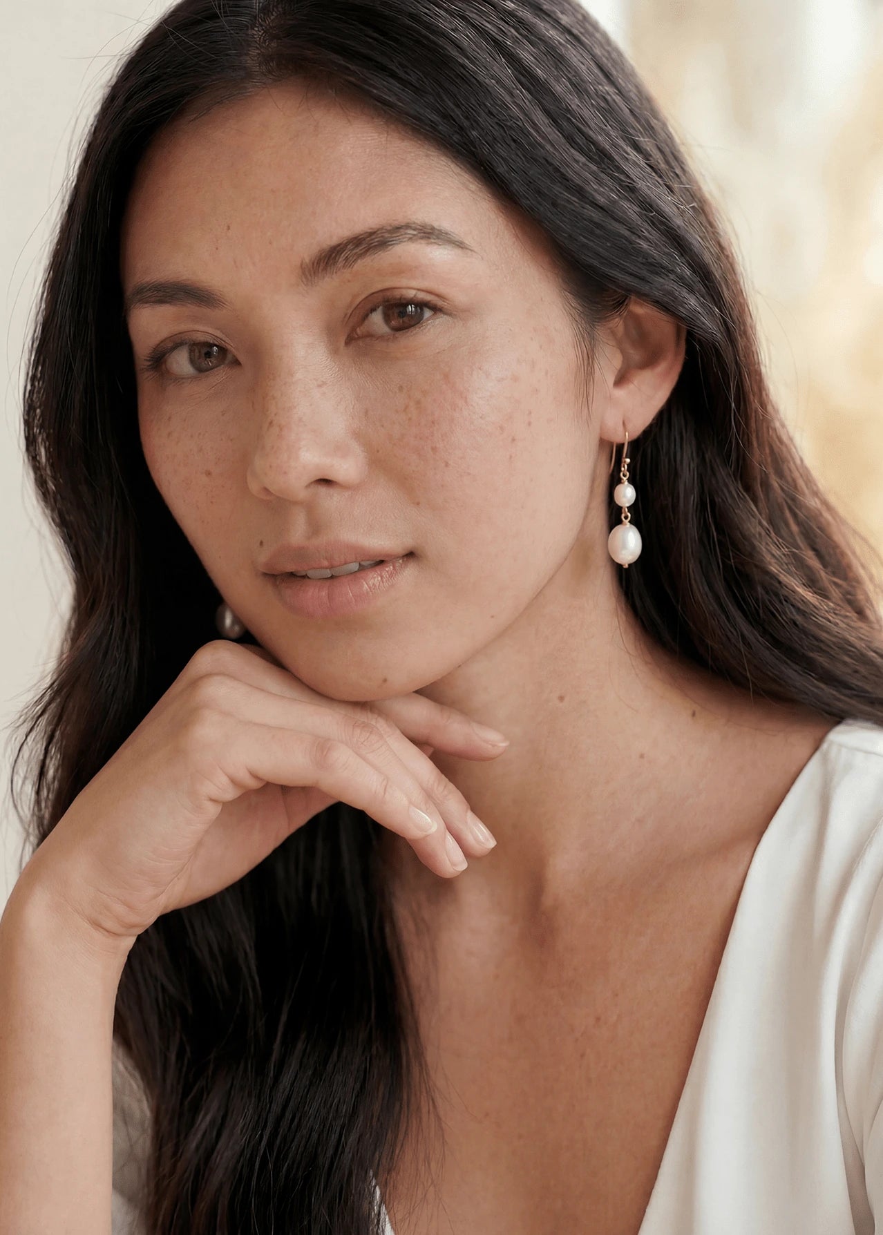 Filipino woman with gold-filled freshwater pearl earrings handmade by Canadian jewellery designer against neutral background.