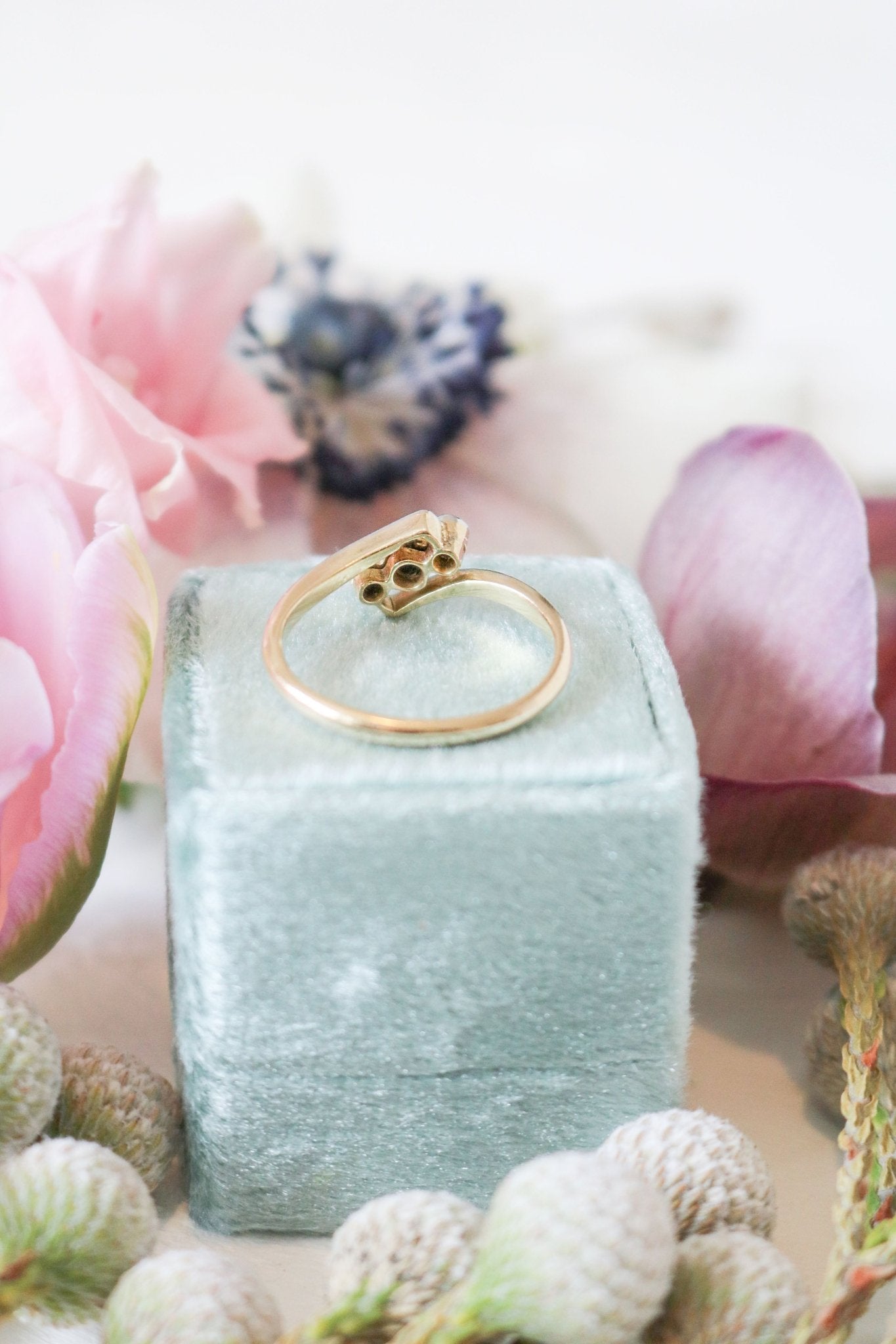 Back view of the Harper Art Deco Diamond Trilogy Vintage Engagement Ring in 18ct Gold and Platinum on a seafoam green ring box surrounded by flowers. Antique Engagement Rings Canada. Canadian vintage engagement rings. Vintage engagement rings Canada. Bridal jewelry Canada. Canadian weddings. Wedding Canada. Canadian bridal jewelry. Woman-owned Canadian jewelry brand. Canadian jewelry business.