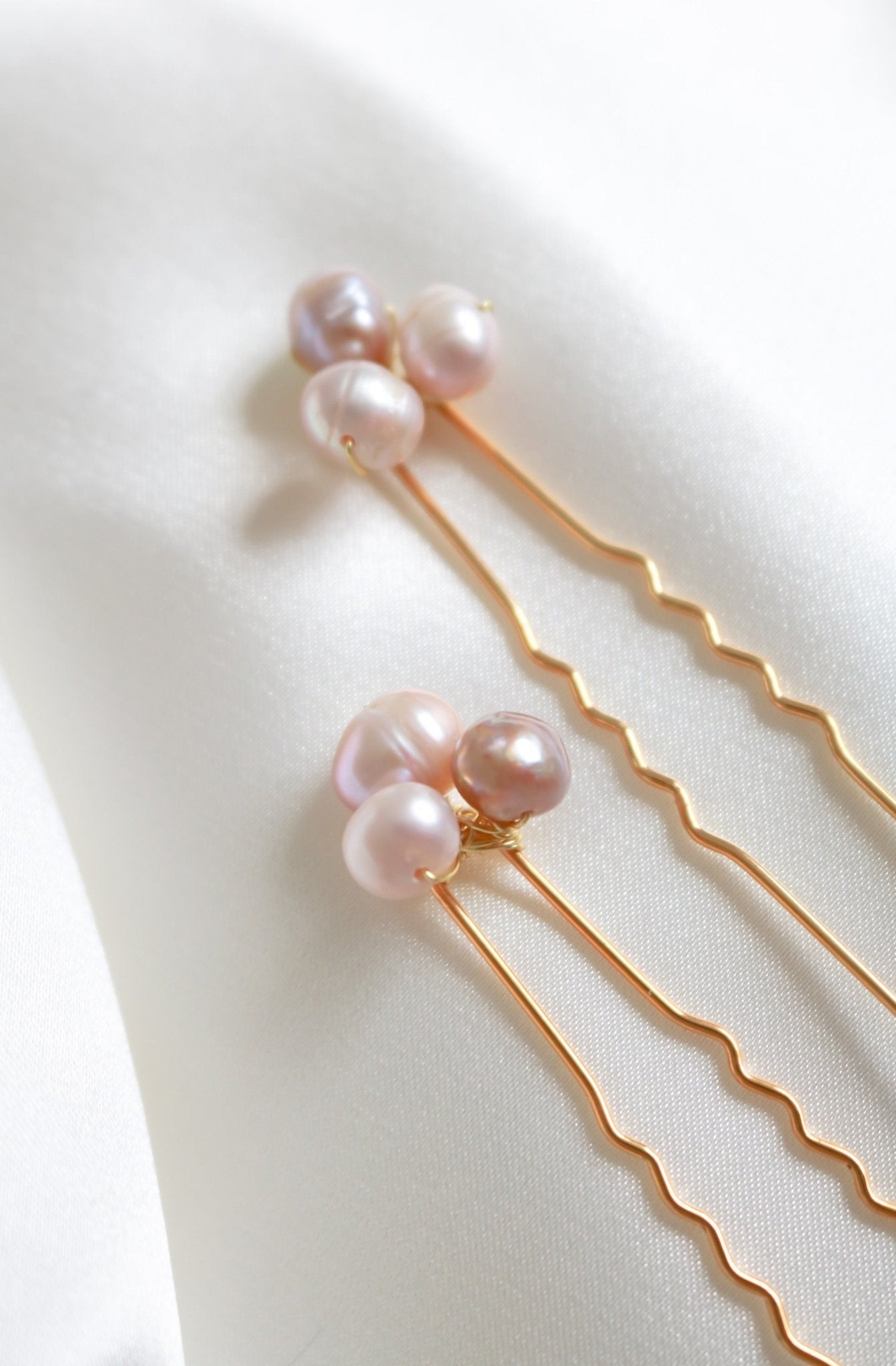 Extreme close up of gold bridal hairpins with freshwater blush pearls on white fabric surface. Handmade bridal accessories & bridal hair accessories by Canadian BIPOC designer