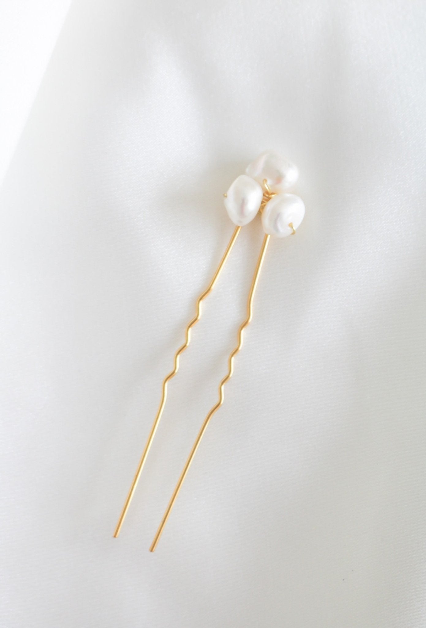 A single gold bridal hairpin with three white freshwater pearls on a white fabric surface. Minimalist bridal jewelry & pearl bridal accessories handmade in Canada by BIPOC jewelry designer