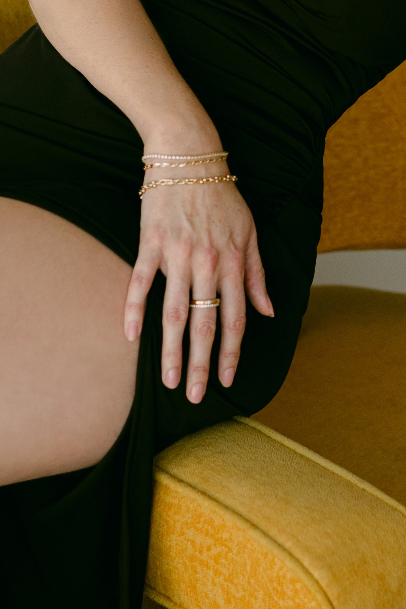 Close-up of a hand with gold-filled jewelry on a yellow cushioned chair. Canadian jewelry brands. Handmade Canadian jewelry.