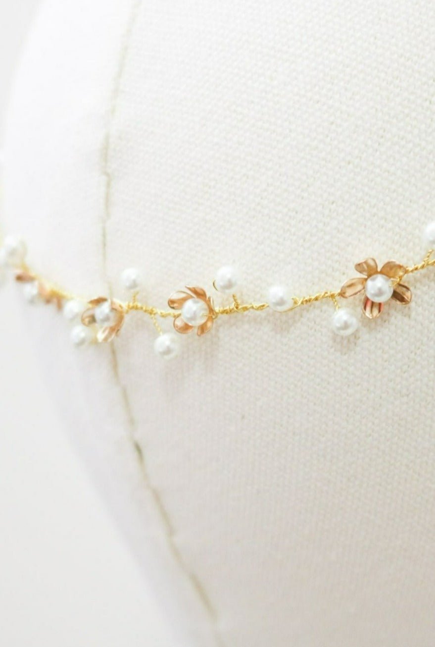 An extreme close up of a gold floral bridal hairvine with Swarovski pearls displayed on a head bust. Handmade bridal accessories & pearl bridal accessories by BIPOC bridal designer