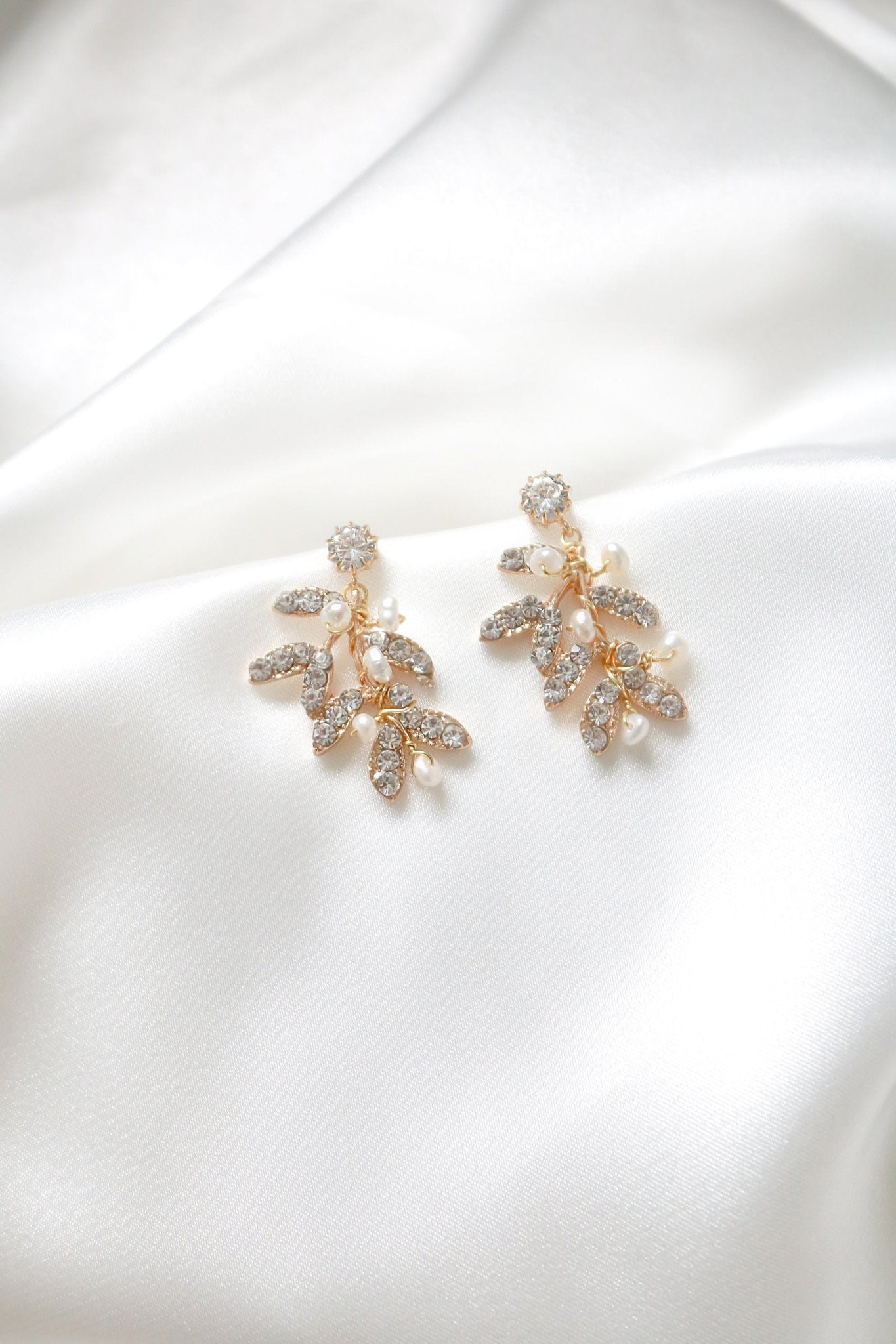 A pair of gold-filled leafy studs with crystals and freshwater pearls sitting on a background of white satin. Canadian jewelry designs. Bridal jewelry Canada. Pearl jewelry Canada. Pearl Bridal jewelry Canada. Gold-filled jewelry Canada. Gold-filled Canadian jewelry. Canadian jewelry brands. Canadian bridal jewelry. Woman-owned Canadian jewelry brand. Statement Earrings. Statement Bridal Earrings. Handmade Canadian jewelry.