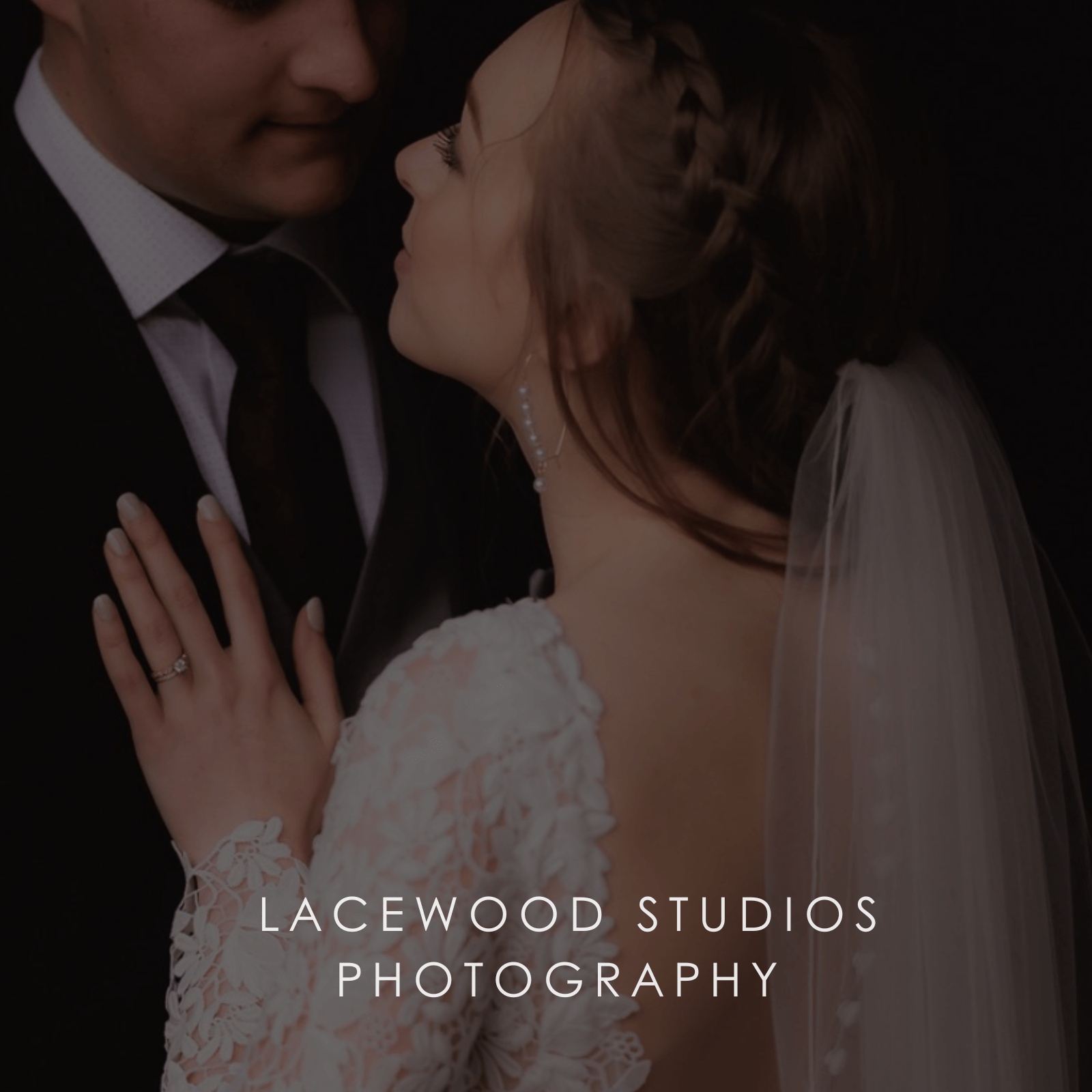 A bride in a floral lace wedding dress and tulle veil lays her hand on her groom's chest.