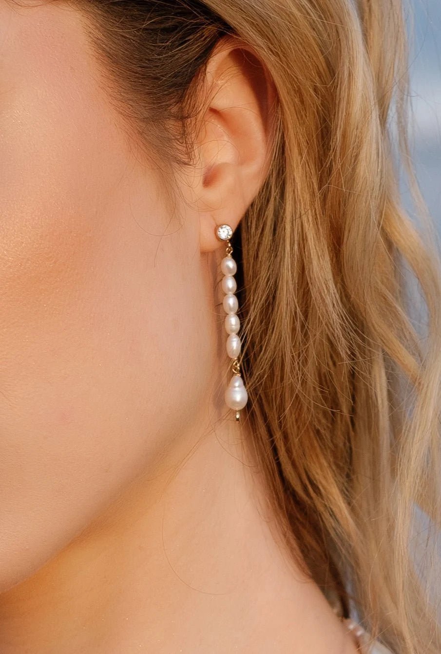 A close up of a gold-filled freshwater pearl drop bridal earring with crystal stud dangling from a bride's ear. Canadian handmade pearl jewelry & freshwater pearl jewelry by BIPOC jewelry designer