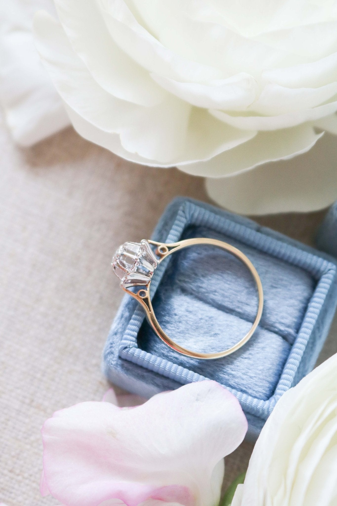 A close up view of the Liona Floral Vintage Engagement Ring in 14ct Gold, Art Deco Style c.1920s. Ring sitting on a blue ring box surrounded by white roses. Antique Engagement Rings Canada. Canadian vintage engagement rings. Vintage engagement rings Canada. Bridal jewelry Canada.