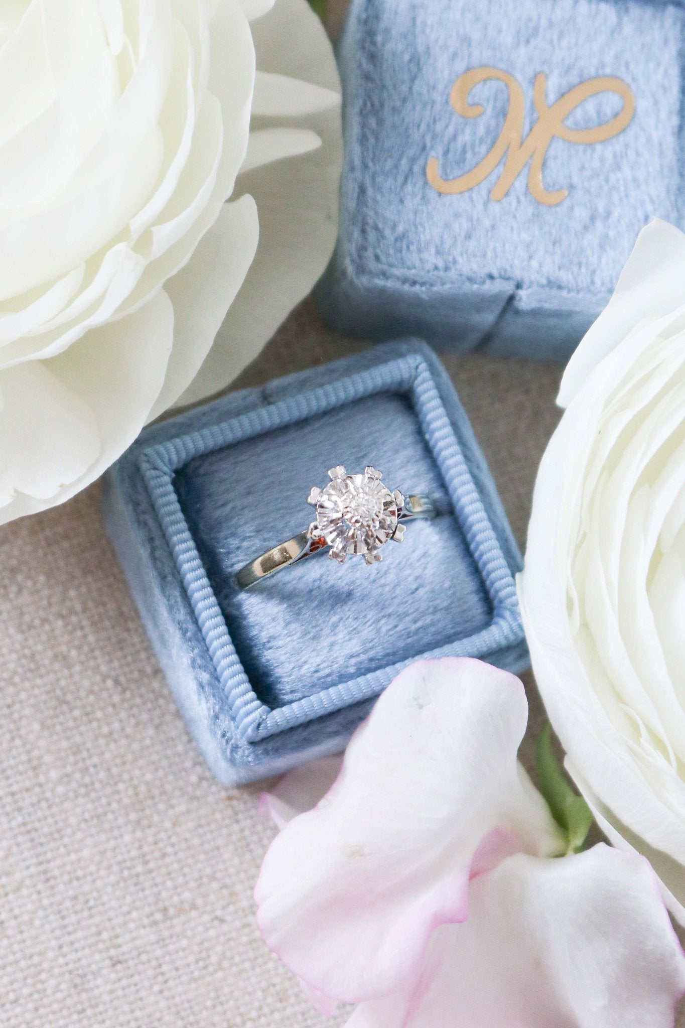 The Liona Floral Vintage Engagement Ring in 14ct Gold, Art Deco Style c.1920s. Ring sitting in a blue ring box surrounded by white roses. Antique Engagement Rings Canada. Canadian vintage engagement rings. Vintage engagement rings Canada. Bridal jewelry Canada.