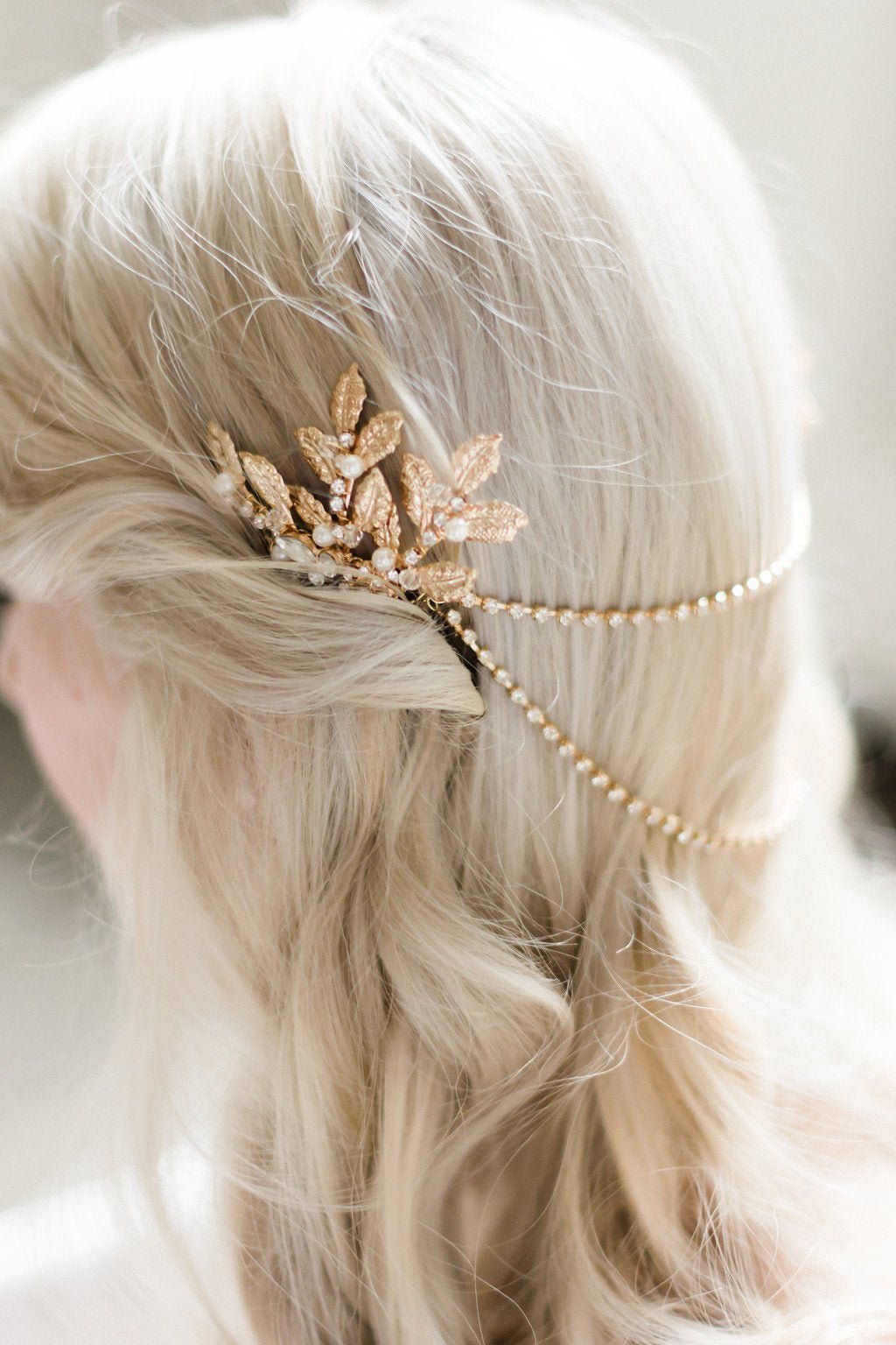 A gold leafy bridal hairpiece with crystals and pearls tucked into wavy blonde locks with blurred background. Bridal hair accessories & pearl accessories Canada