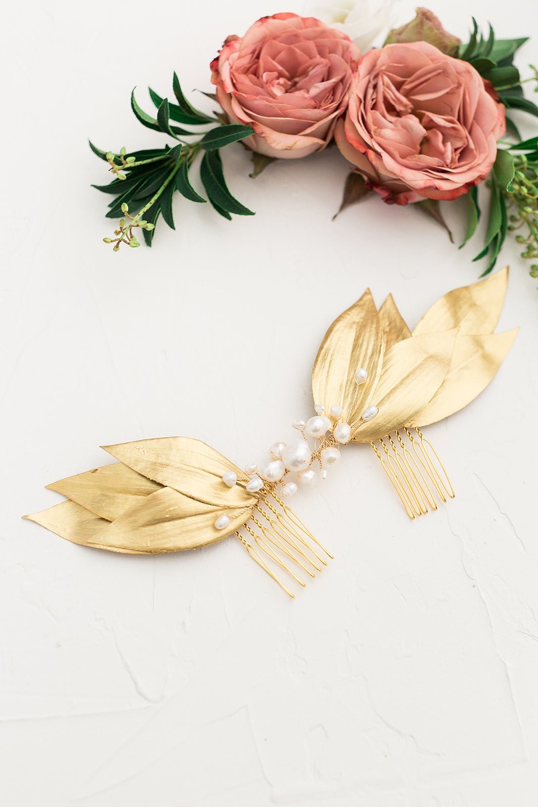 A golden leafed bridal hairpiece with freshwater pearls on a white background with dusty roses. Handmade bridal accessories & Canadian bridal hair accessories by BIPOC wedding designer