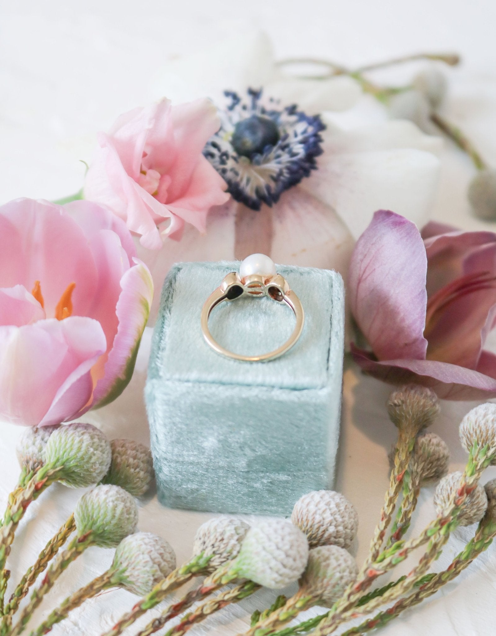 The Luna Diamond and Pearl Vintage Engagement Ring in 9ct Gold on top of a ring box surrounded by flowers. Canadian jewelry designs. Antique Engagement Rings Canada. Canadian vintage engagement rings. Vintage engagement rings Canada. Bridal jewelry Canada. Pearl jewelry Canada. Pearl Bridal jewelry Canada. Canadian jewelry brands. Organic pearl jewelry.