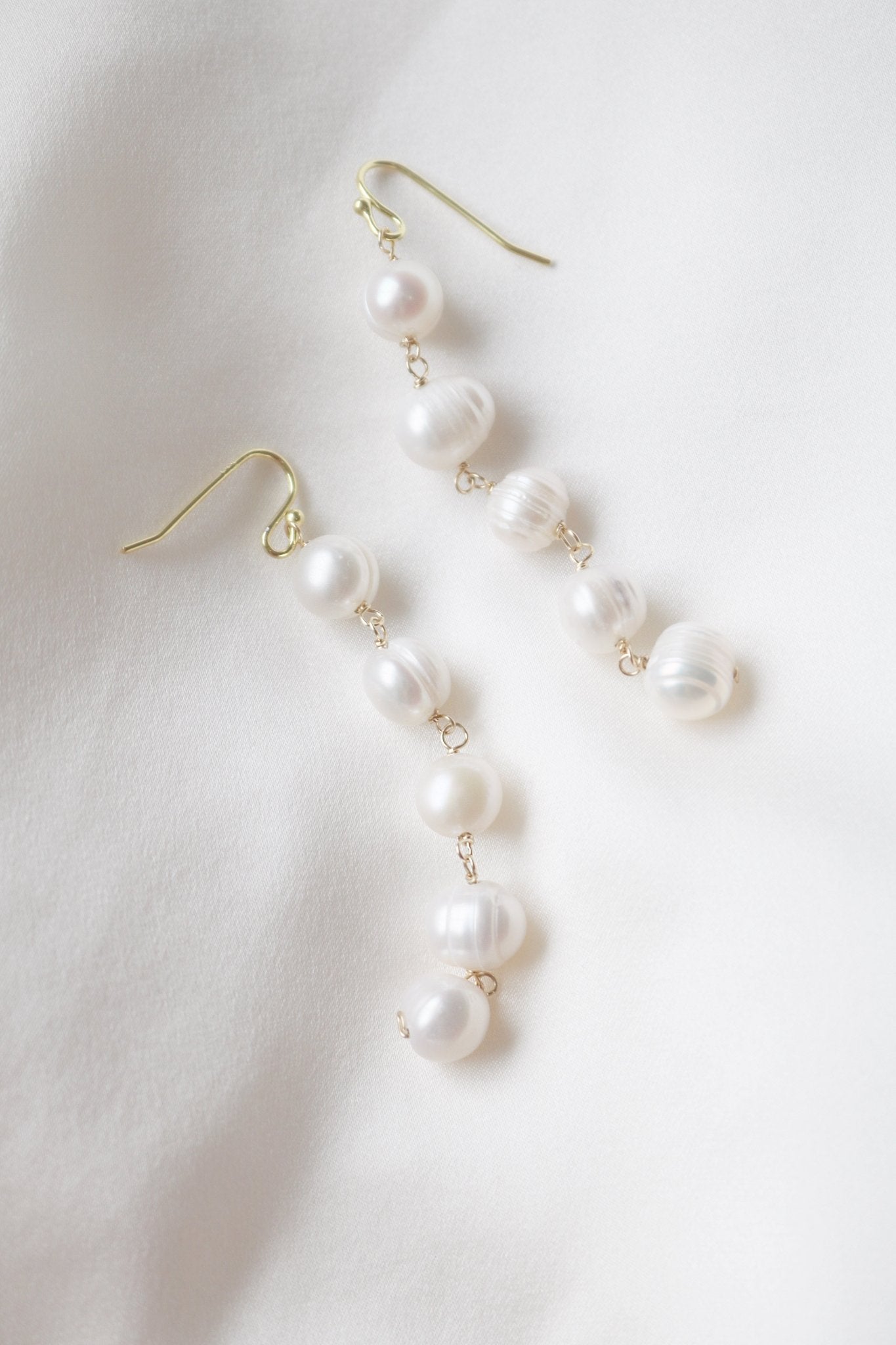 A pair of Maisie Long Statement Fresh Water Pearl Earrings on a white satin background. Bridal jewelry Canada. Pearl jewelry Canada. Pearl Bridal jewelry Canada. Organic pearl jewelry. Gold-filled jewelry Canada. Canadian weddings. Wedding Canada. Canadian jewelry designer.