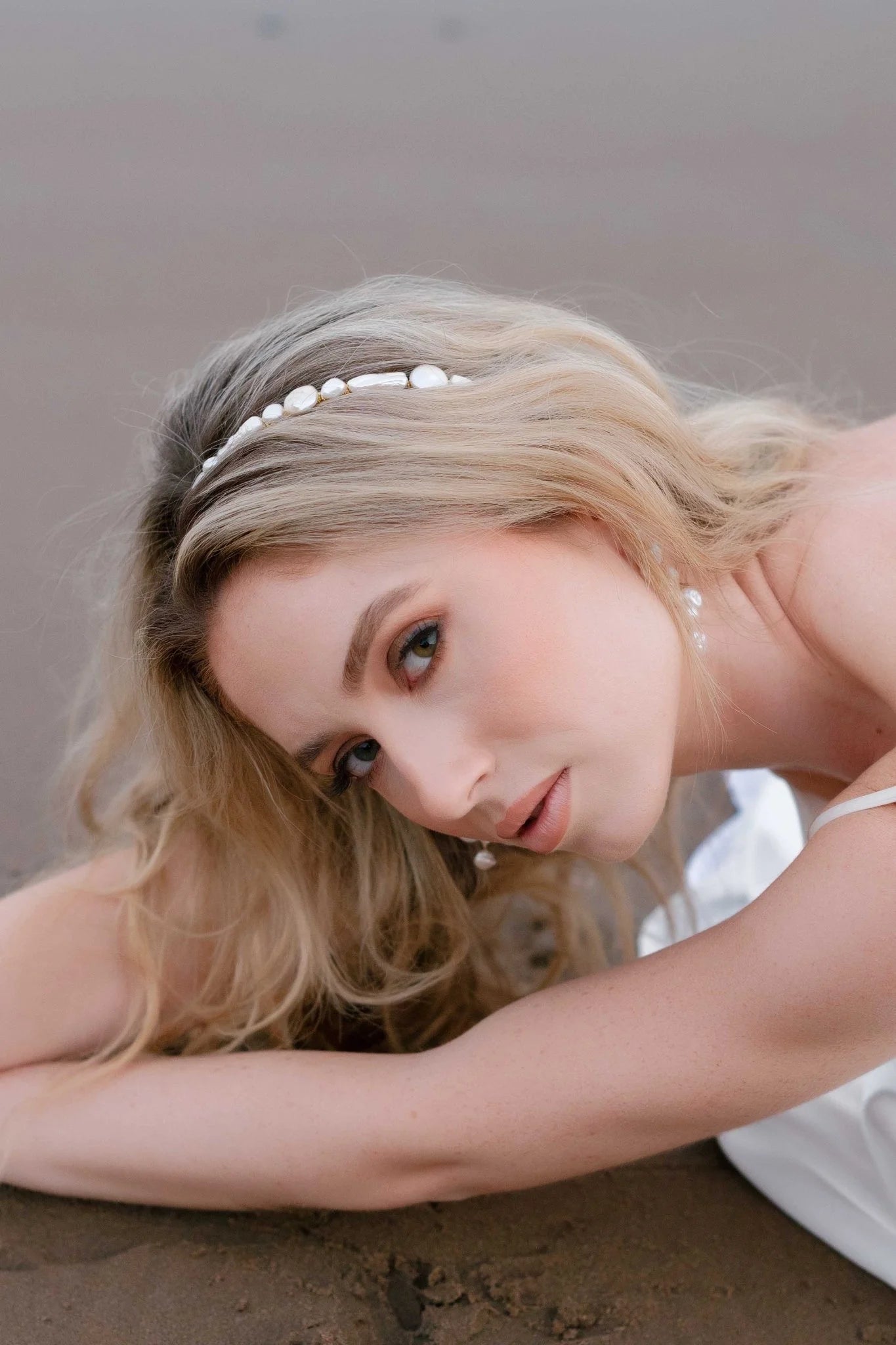 A freshwater pearl bridal headband in a bride's golden hair as she leans over sand at the beach. Handmade bridal accessories, Canadian bridal accessories, & pearl bridal hair accessories by Canadian BIOC bridal designer