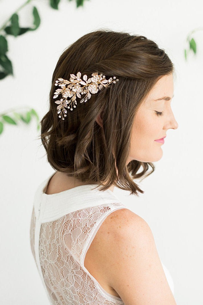 Bride in white lacey wedding dress wearing a gold decorative floral, crystal bridal hairpiece with a few green leaves on a white background. Bridal hair accessories, Canadian wedding accessories, & handmade wedding hair accessories Canada