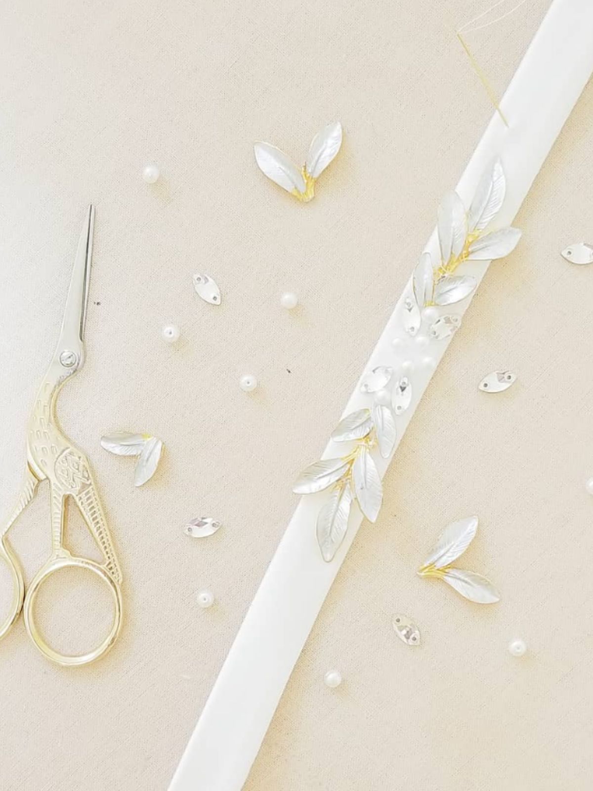 Decorative ribbon with crystal floral embellishments and sewing tools on a light beige background with pearls.