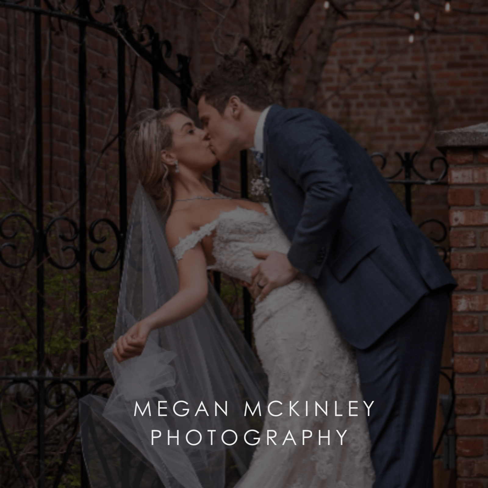 A groom dips his bride for a passionate kiss while she holds the end of her tulle wedding veil.