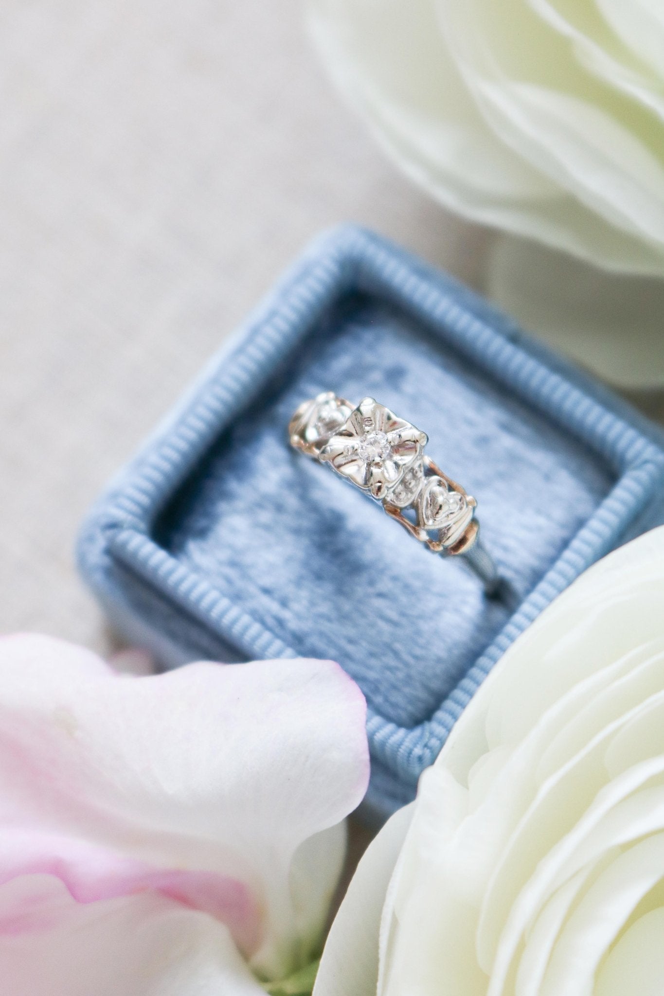 The Melisma Art Deco Diamond Heart Engagement Ring in 14ct Yellow and White Gold sitting in a blue ring box surrounded by white roses. Antique Engagement Rings Canada. Canadian vintage engagement rings. Vintage engagement rings Canada. Bridal jewelry Canada. Canadian weddings. Wedding Canada. Canadian bridal jewelry. Woman-owned Canadian jewelry brand. Canadian jewelry business.
