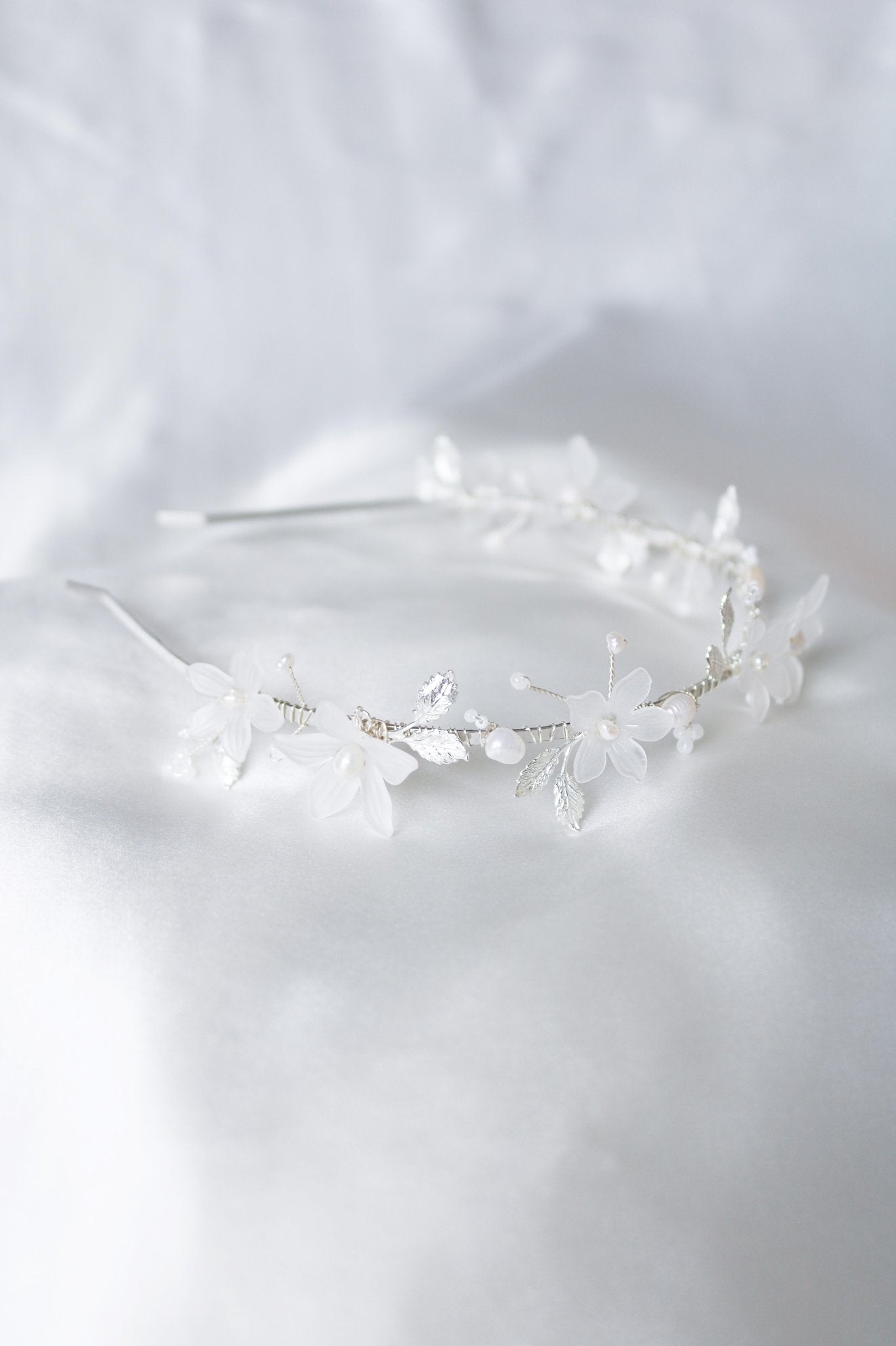 Side view of a silver floral bridal headband with organic freshwater pearls laying on a satin sheet. Bridal Hair Accessories. Bridal Accessories. Canadian Bridal Accessories. Handmade Canadian Accessories. Canadian handmade Accessories. Organic pearl accessories. Canadian weddings. Wedding Canada.