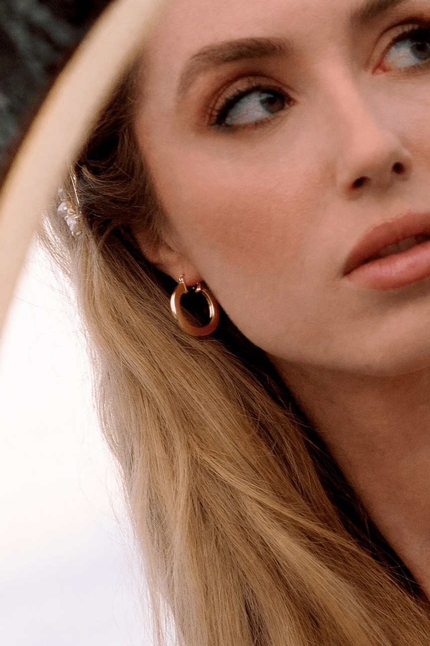 Close-up of a woman wearing gold hoop earrings with a blurred background. Gold-filled Canadian jewelry. Affordable jewelry. Handmade Canadian jewelry. Everyday jewelry. Minimalist Jewelry.