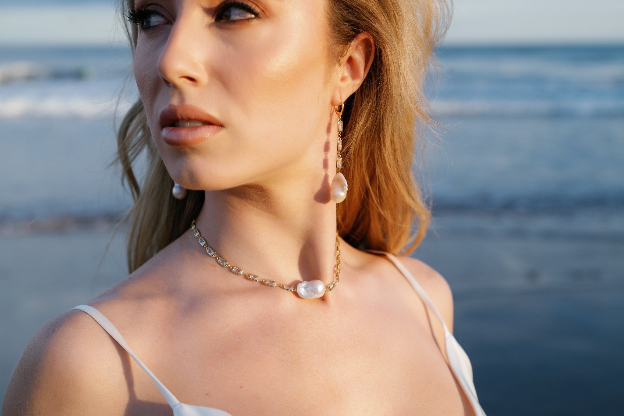 A bride looks away while wearing a gold-filled crystal baroque freshwater pearl necklace and matching dangle earrings. Canadian jewelry brands. Pearl Bridal jewelry Canada. Organic pearl jewelry. Pearl jewelry sets. Statement Earrings. Statement Bridal Earrings. Canadian bridal jewelry. Canadian jewelry brands. Gold-filled jewelry Canada. Gold-filled Canadian jewelry. Bridal jewelry Canada. Pearl jewelry Canada.