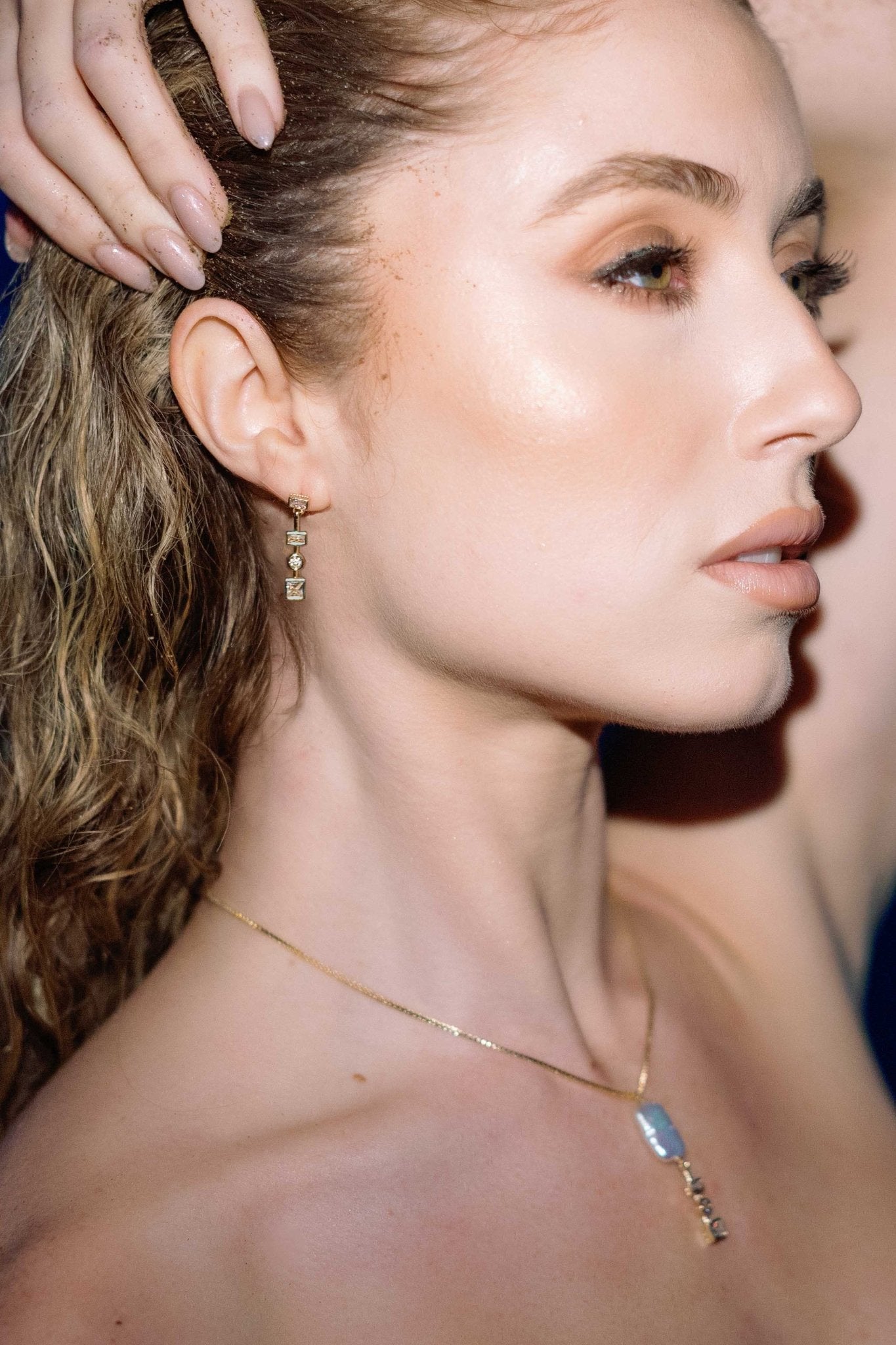 Close-up of a woman's face holding her hair back with gold-filled crystal earrings and matching necklace. Matching jewelry set, modern jewelry designs, & everyday jewelry handmade by Canadian BIPOC jewelry designer