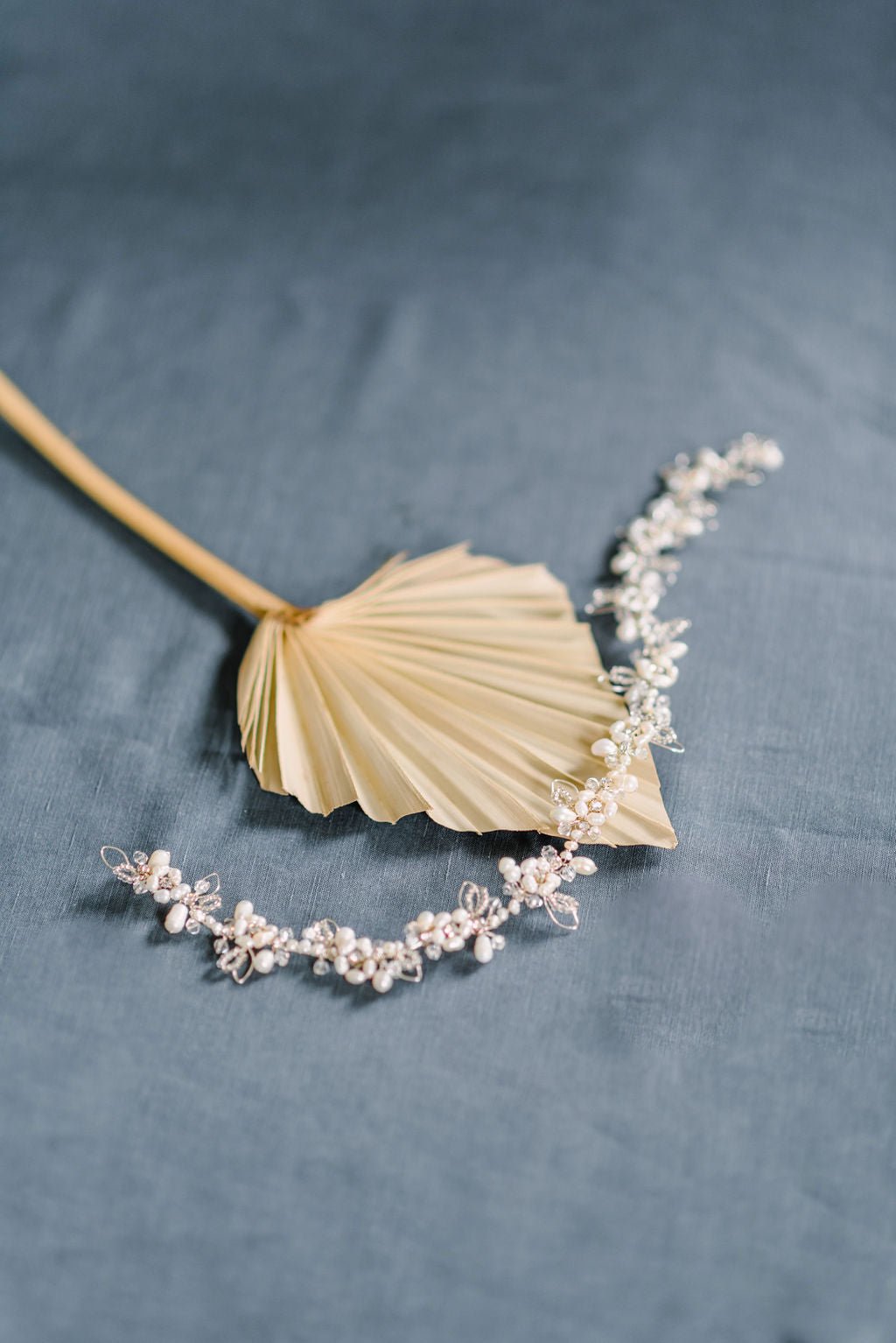 The Nevah Floral Fresh Water Pearl and Crystal Hairvine lays across a golden leaf on a blue background. Bridal Hair Accessories. Bridal Accessories. Canadian Bridal Accessories. Handmade Canadian Accessories. Canadian handmade Accessories. Canadian weddings. Wedding Canada.