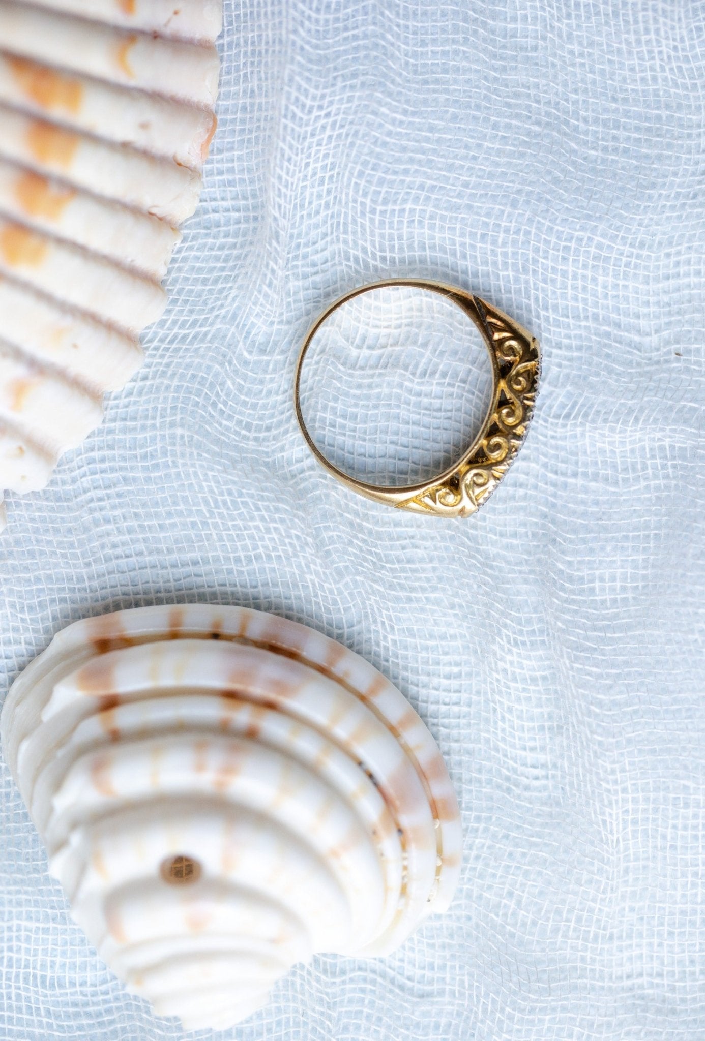 A close up of the side view of a 18k gold diamond vintage engagement ring with seashells on a pale blue fabric. Antique Engagement Rings Canada. Canadian vintage engagement rings. Vintage engagement rings Canada. Bridal jewelry Canada. Canadian weddings. Wedding Canada. Canadian bridal jewelry. Woman-owned Canadian jewelry brand. Canadian jewelry business.