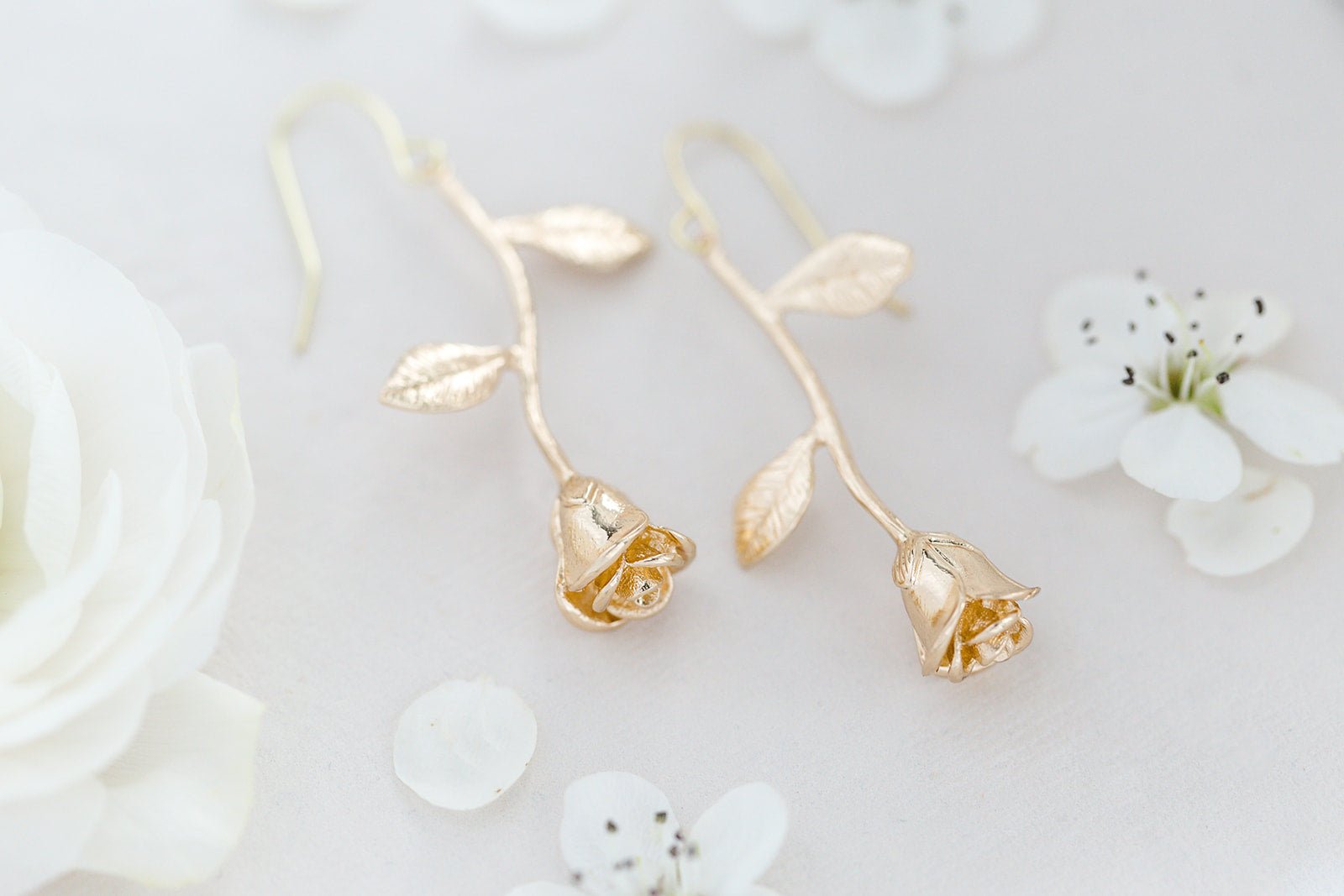 A pair of 14k Gold-filled Orarose Golden Rose Earrings on white background surrounded by white flowers.