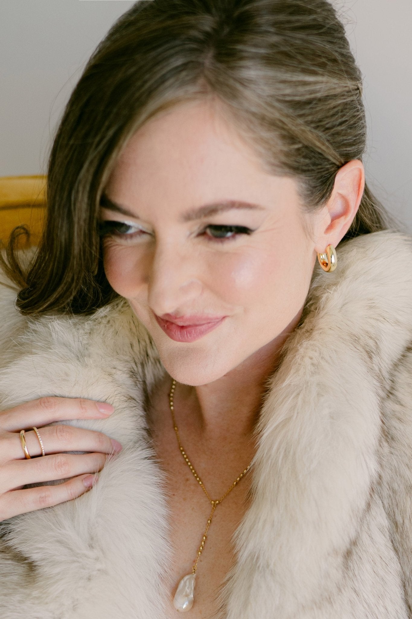 Woman with fur coat wearing puffy gold earrings and gold beaded lariat necklace with baroque pearl. Canadian handmade jewelry.