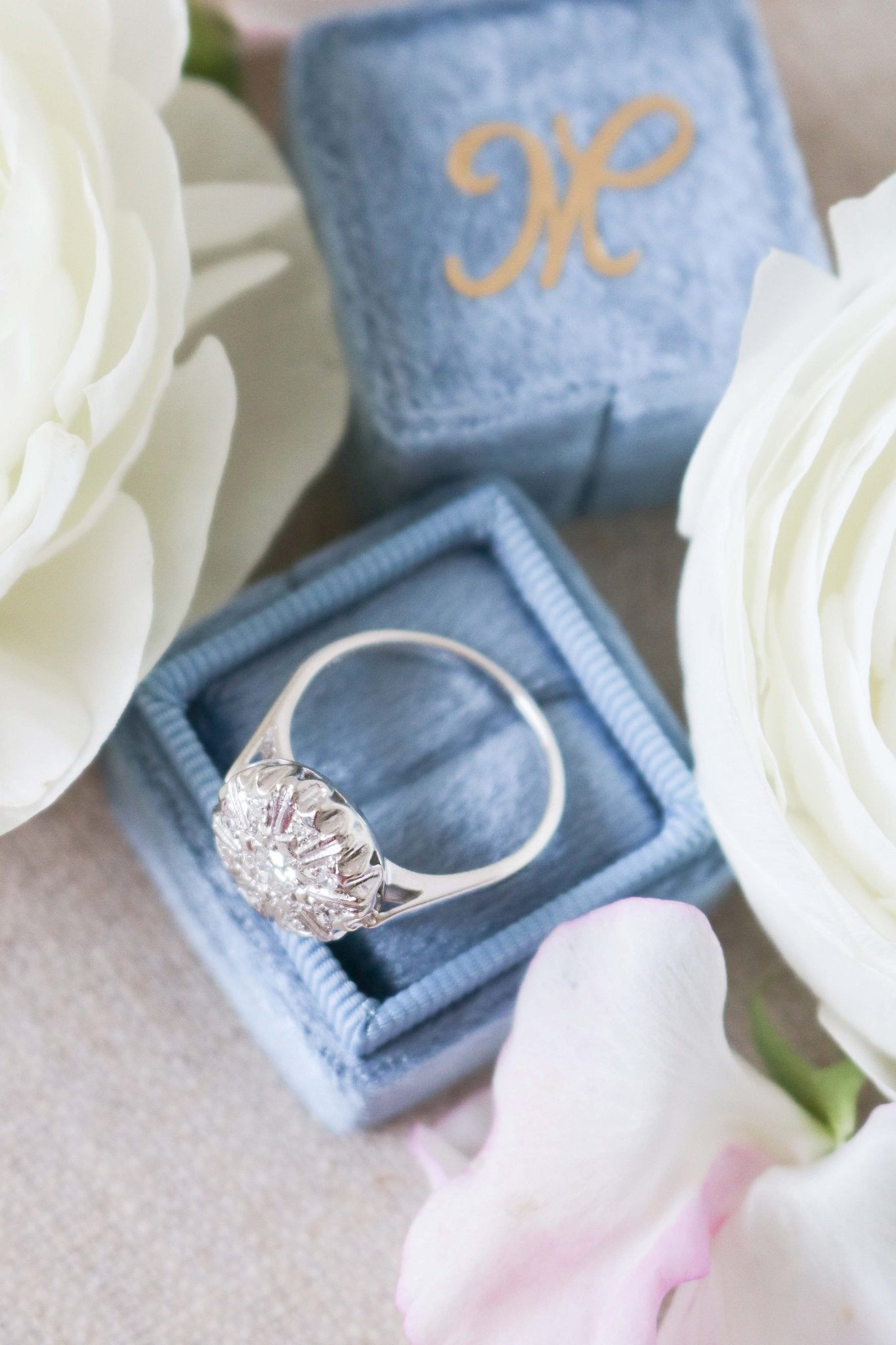 Top view of side of Selene Art Deco 14k White Gold Diamond Vintage Engagement Ring on top of blue ring box surrounded by white roses. Canadian vintage engagement rings. Bridal jewelry Canada. Vintage engagement rings Canada. Canadian weddings. Wedding Canada. Woman-owned Canadian jewelry brand. Canadian jewelry business. Small Canadian jewelry brands.
