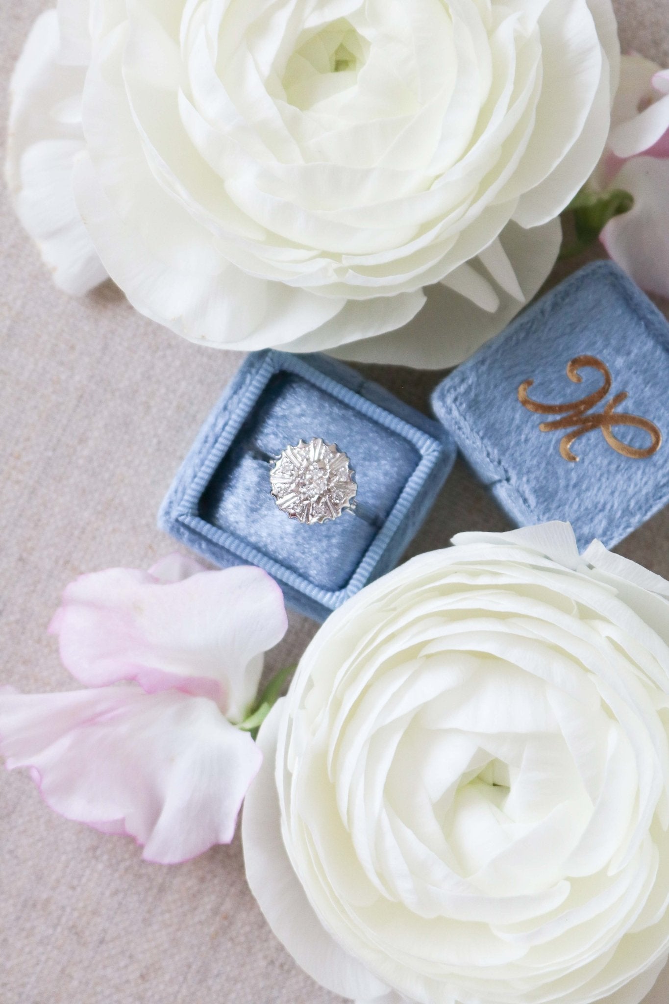Top view of Selene Art Deco 14k White Gold Diamond Vintage Engagement Ring in a blue ring box surrounded by white roses. Canadian vintage engagement rings. Bridal jewelry Canada. Vintage engagement rings Canada. Canadian weddings. Wedding Canada. Woman-owned Canadian jewelry brand. Canadian jewelry business. Small Canadian jewelry brands.