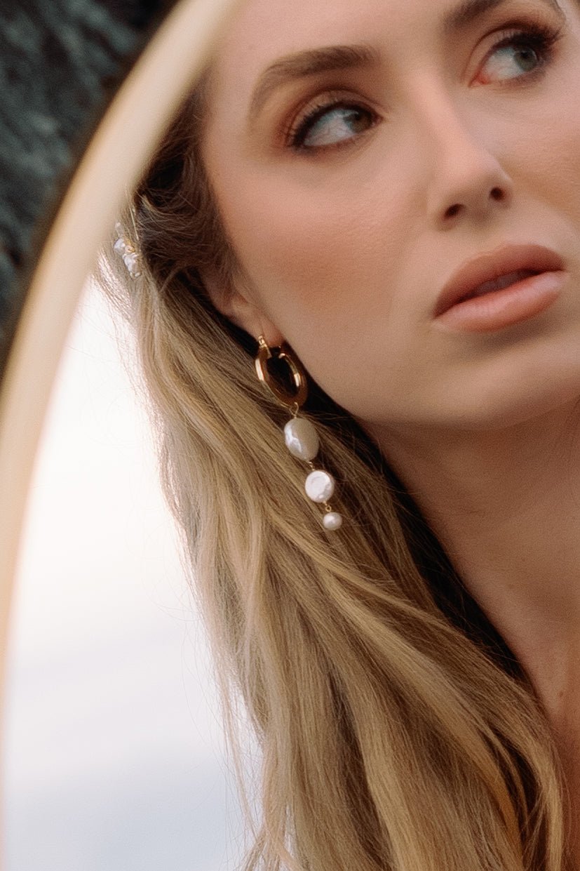 A close up of a mirrored bride looks away while showing off her gold-filled freshwater pearl dangle hoops. Pearl Bridal jewelry Canada. Handmade jewelry Canada
