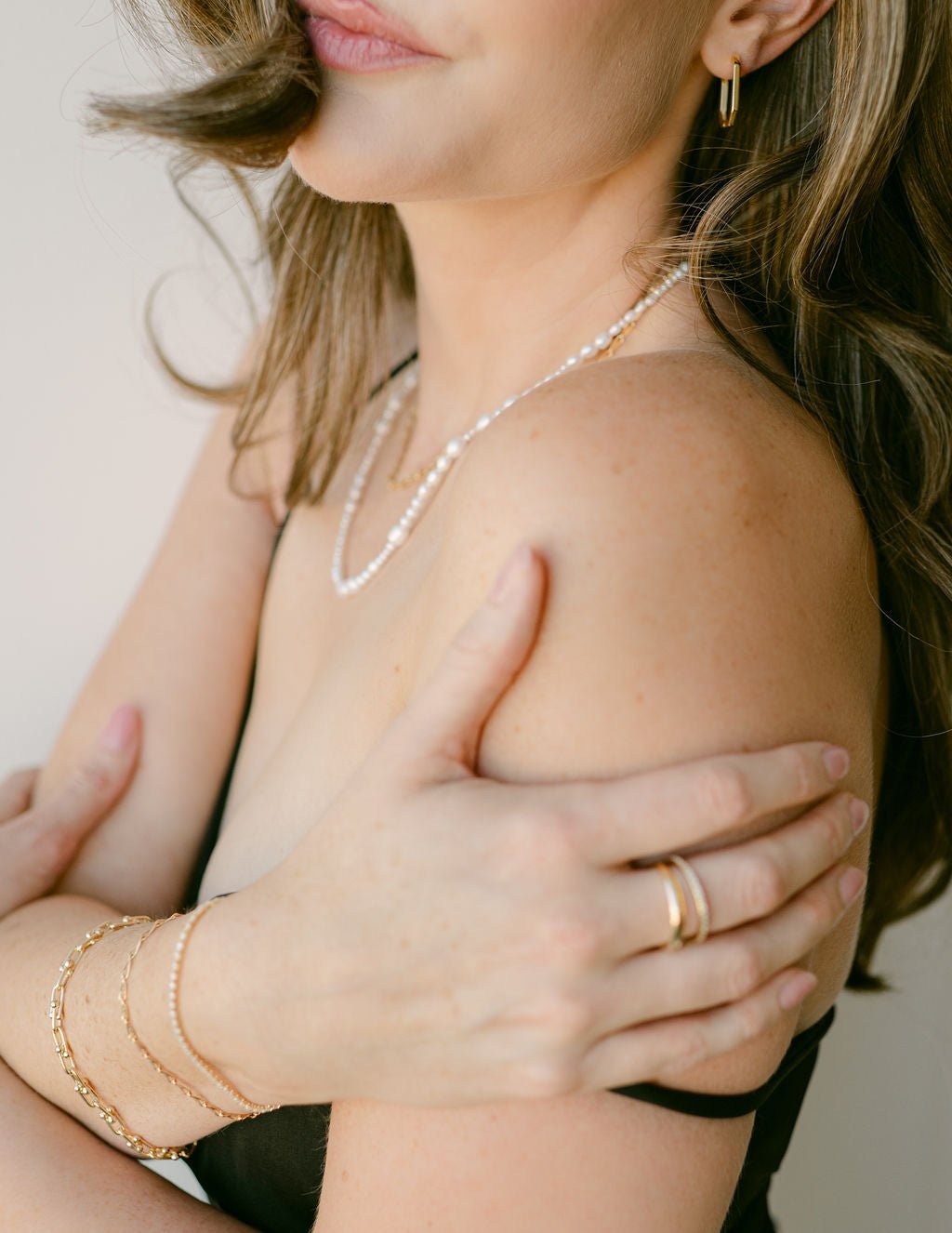 Close-up of a person wearing a freshwater pearl string necklace and gold-filled jewelry including a bracelet stack, and rings. Pearl jewelry Canada.