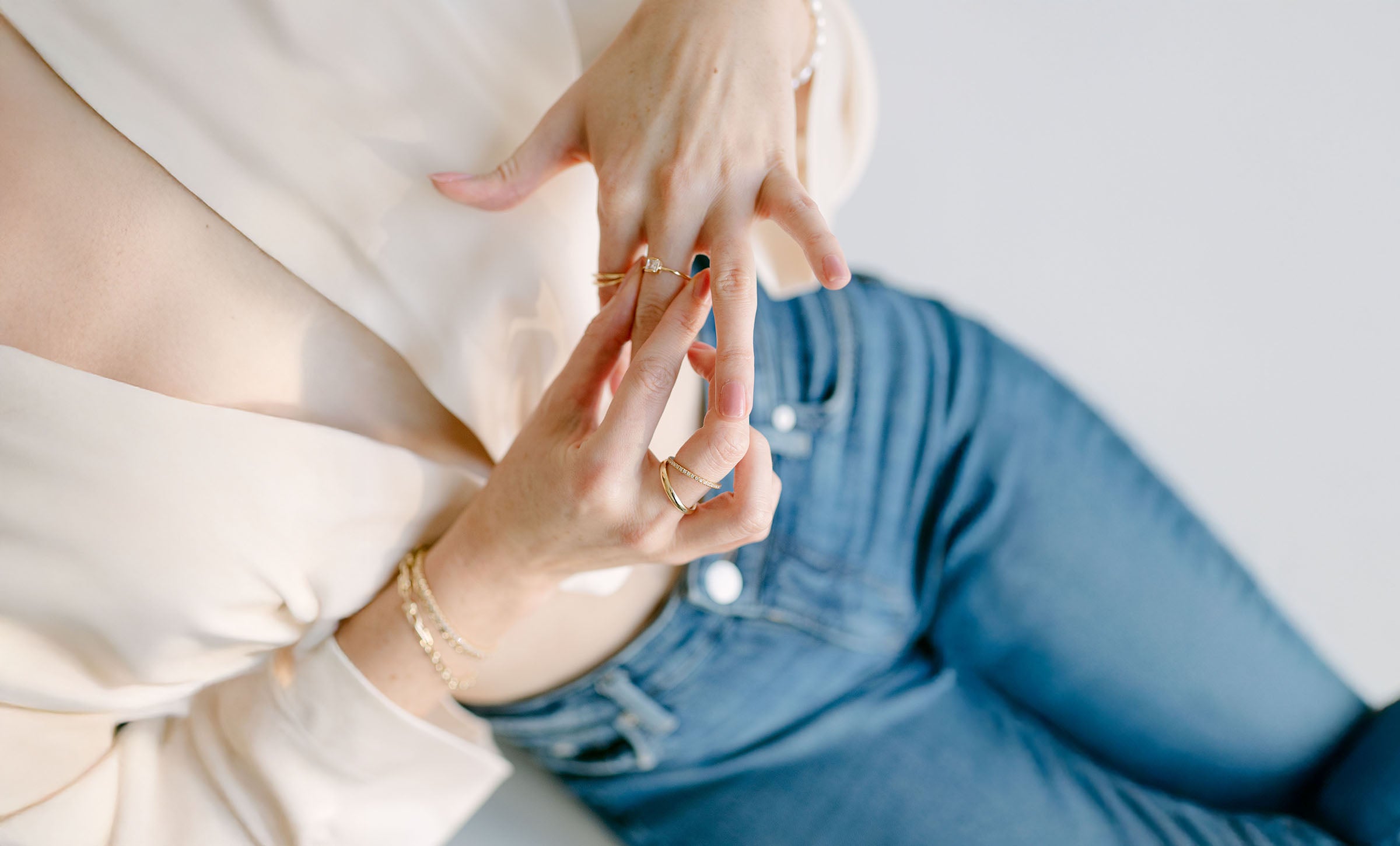 Close up of a woman's hands fiddling with gold filled rings with crystals on white background.