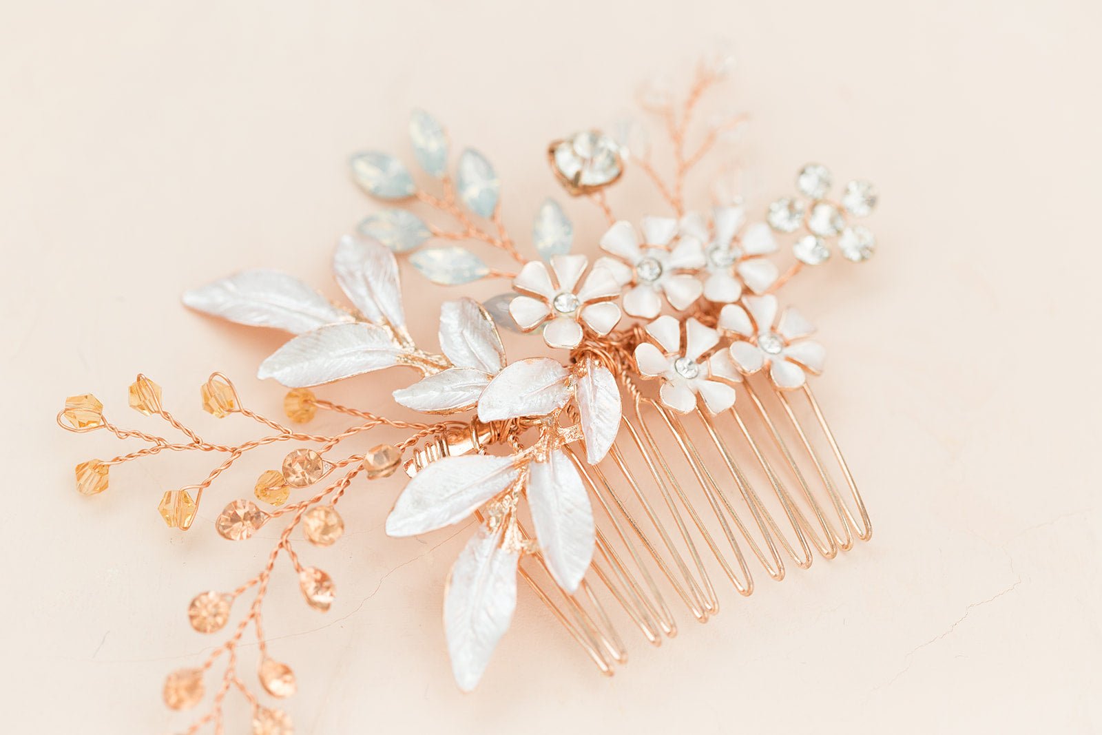 Extreme close up of a rose gold decorative bridal hair comb with enamel florals and crystal leaf details on a light pink background. Canadian bridal accessories, bridal hair accessories, & affordable bridal accessories Canada