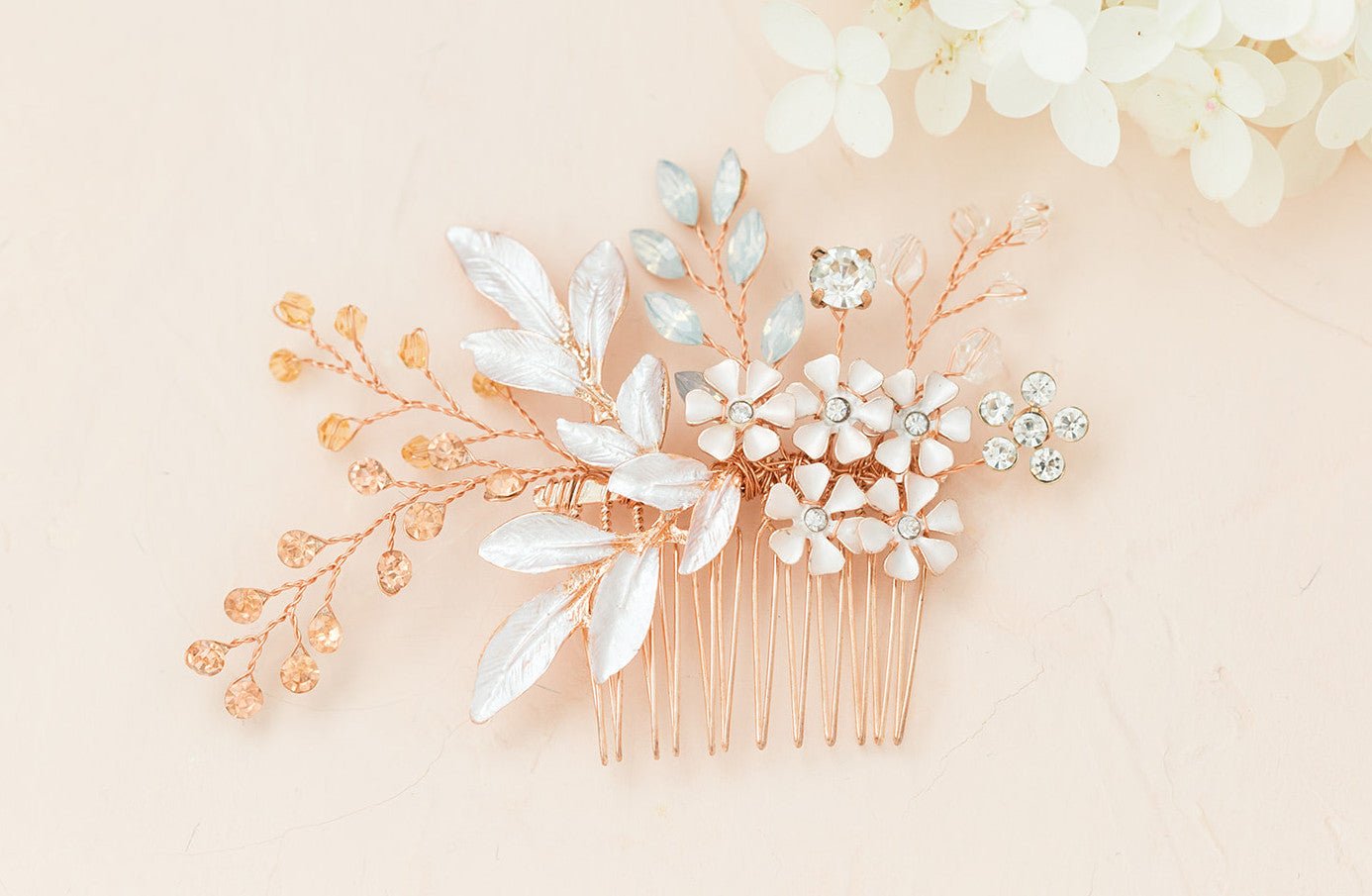 Close up of a rose gold decorative bridal hair comb with enamel flowers and crystal leaf details on a soft pink background. Bridal hair accessories, affordable bridal accessories, & handmade bridal accessories by BIPOC bridal designer