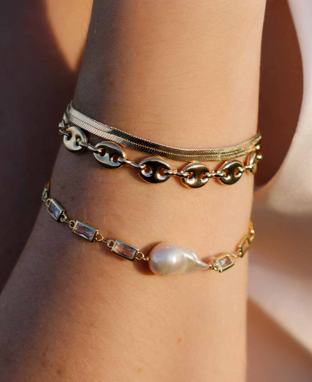 Three gold-filled bracelets: Herringbone, puffy mariner link, and crystal link with baroque freshwater pearl.