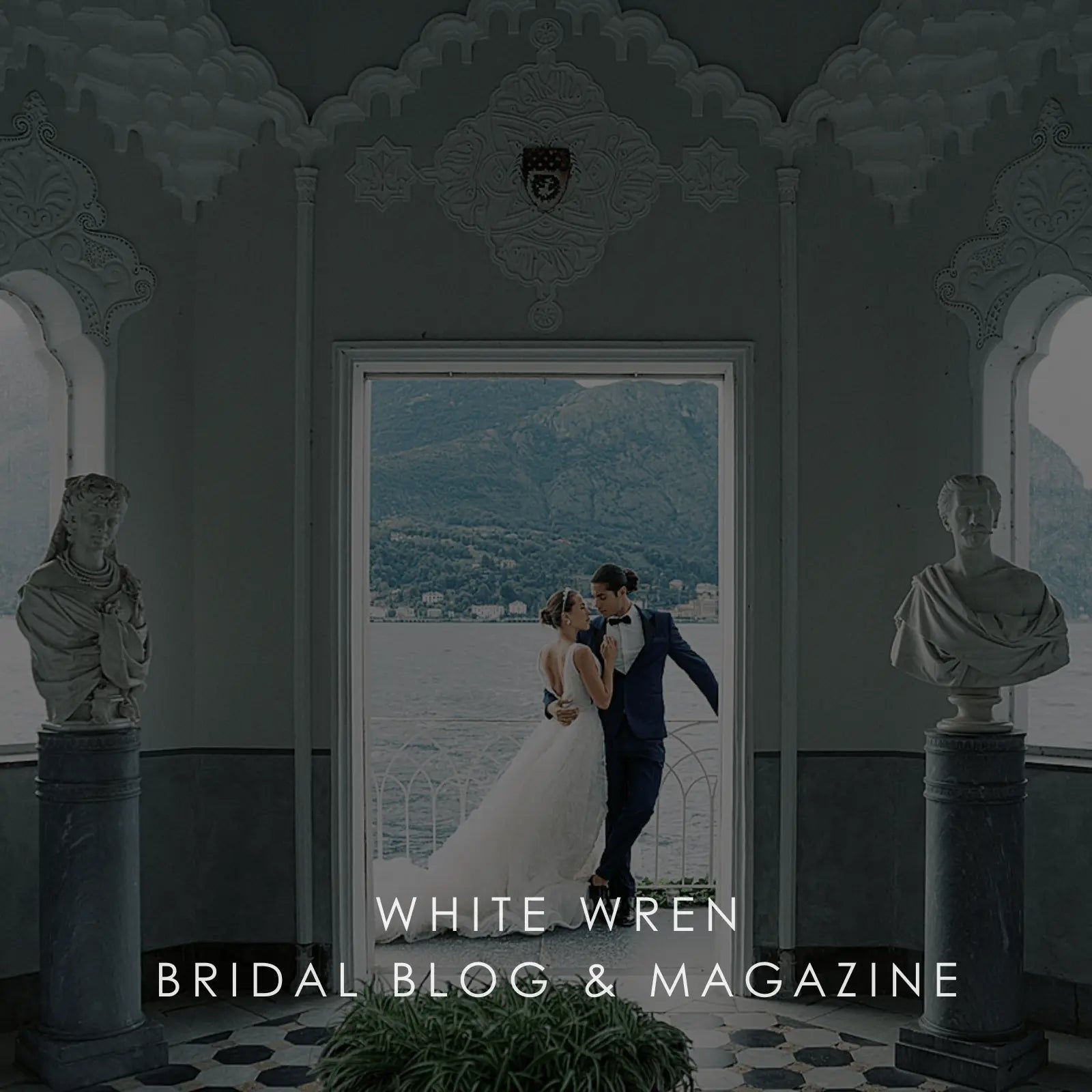Couple in wedding attire standing in a decorative room with statues and a scenic view.
