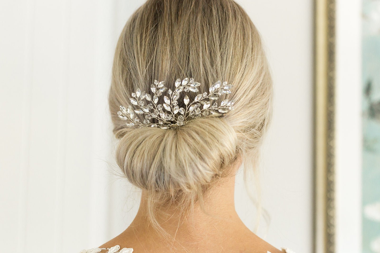 A silver crystal bridal hair comb tucked into a tight blonde bridal bun with blurred background. Bridal Hair Accessories, Canadian Bridal Accessories, & handmade Canadian accessories by BIPOC bridal designer