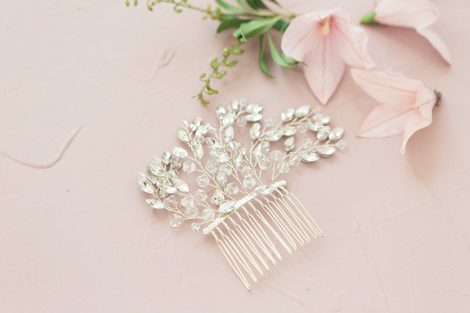 Close up of a silver Crystal leaf Bridal Hair Comb and flowers on pale pink surface. Bridal Hair Accessories, Canadian Bridal Accessories, & Handmade Canadian Accessories by BIPOC bridal designer