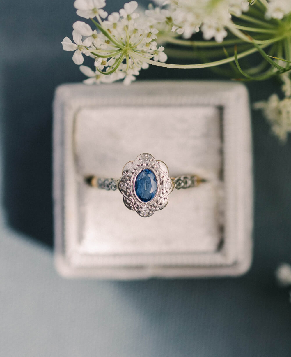 A vintage engagement ring in a ring box with white flowers.
