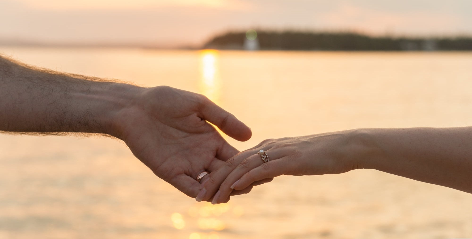 Bride and groom lightly hold hands at sunset by the sea.