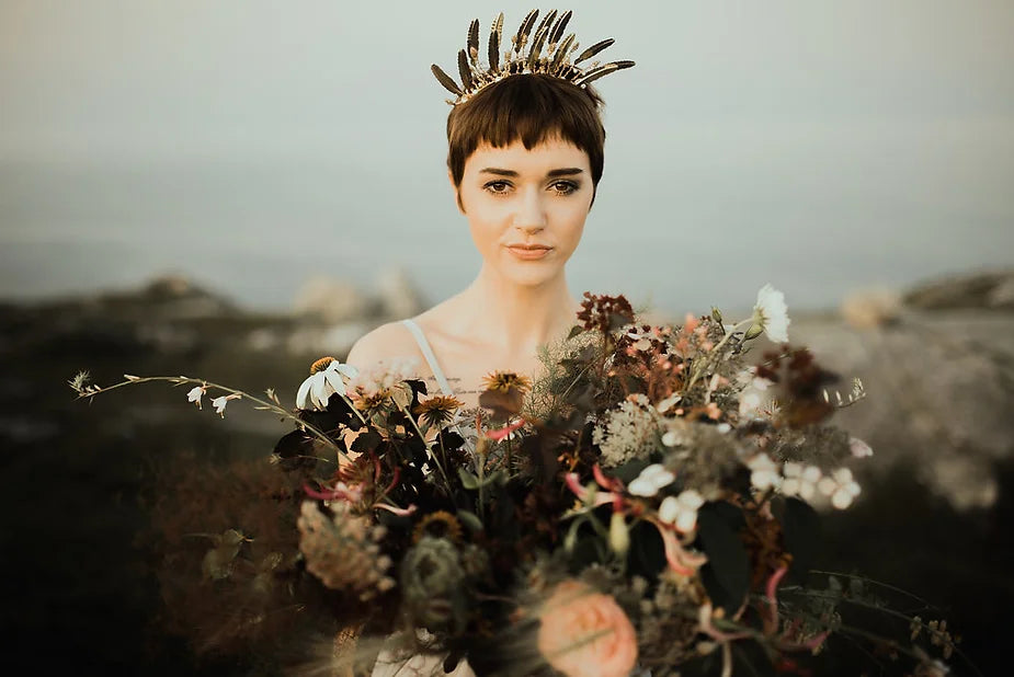 A seaside bride holds a bouquet of wild flowers and flora with the ocean to her back.