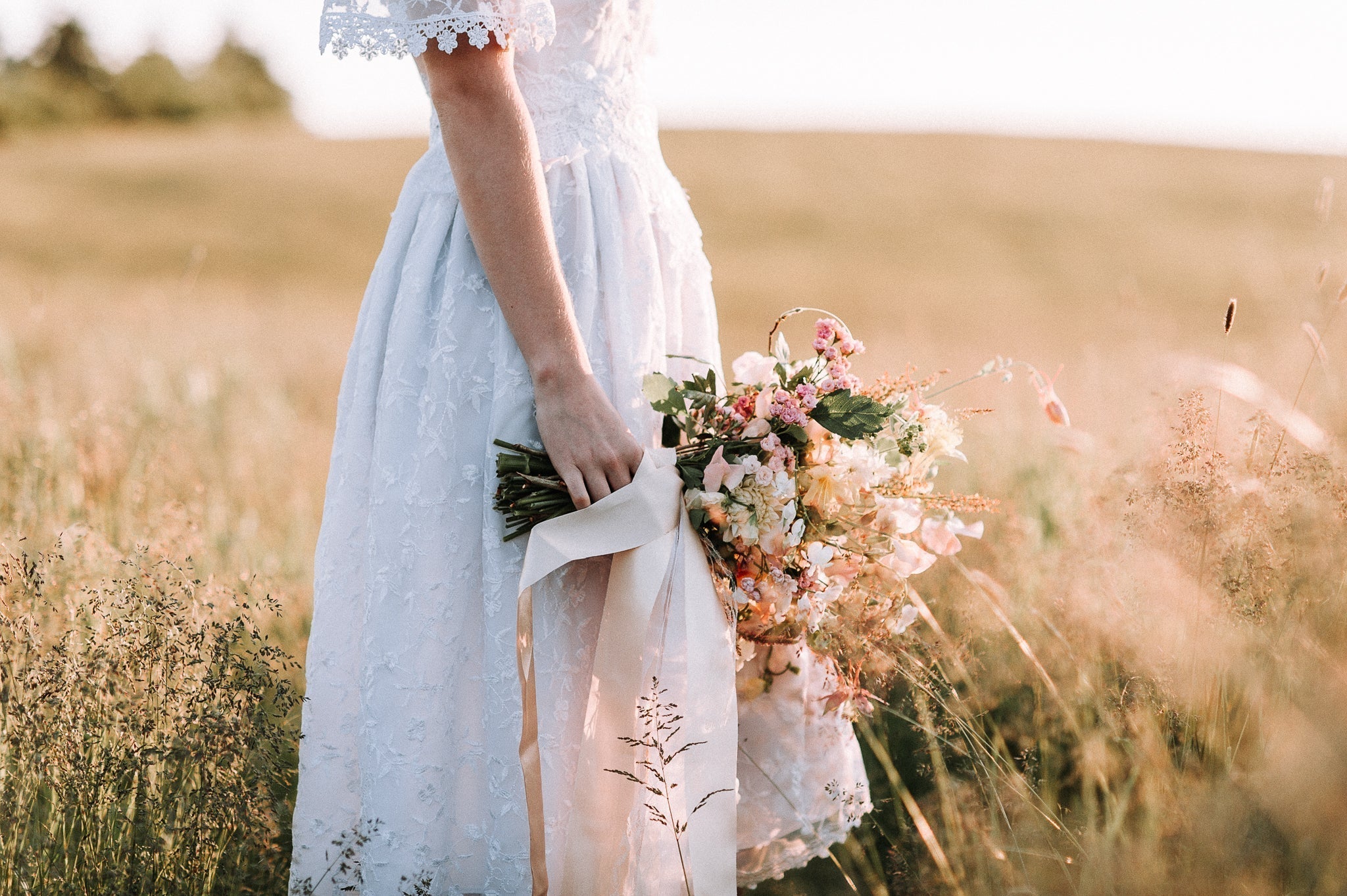 Bottom half of bride standing in a grassy field holding a flower bouquet.